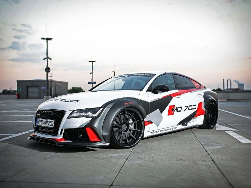 Audi S7 桌布 壁紙 — 一輛白色、紅色和黑色的Audi RS7跑車帶有MD 700塗裝，停在日落時分的混凝土停車場上。