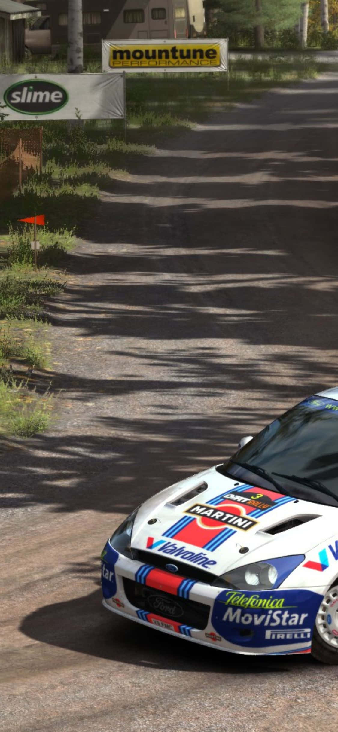 iPhone X Dirt Rally 桌布 壁紙 — 一輛白色、藍色和紅色Martini塗裝的拉力賽車，在陽光斑駁、兩旁掛滿贊助商橫幅和樹木的泥路上飛馳。