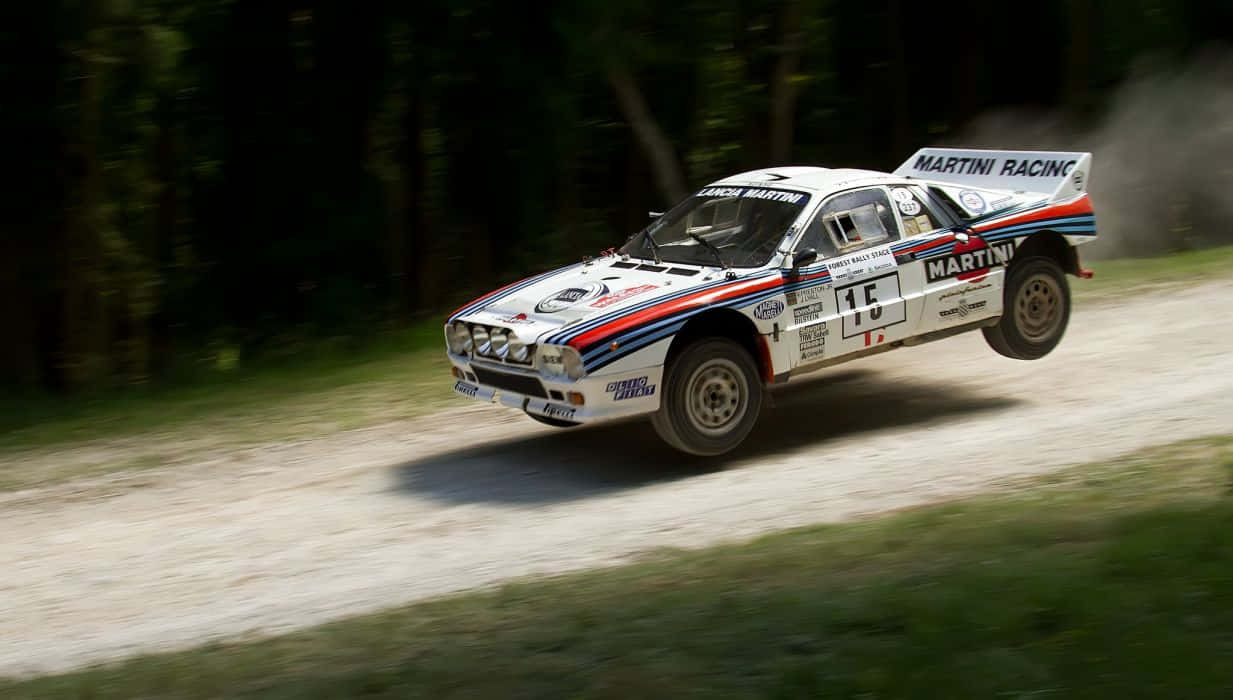 Lancia 桌布 壁紙 — 一輛白色、藍色和紅色的 Martini Racing Lancia Delta S4 拉力賽車在森林泥路上疾馳，揚起灰塵。