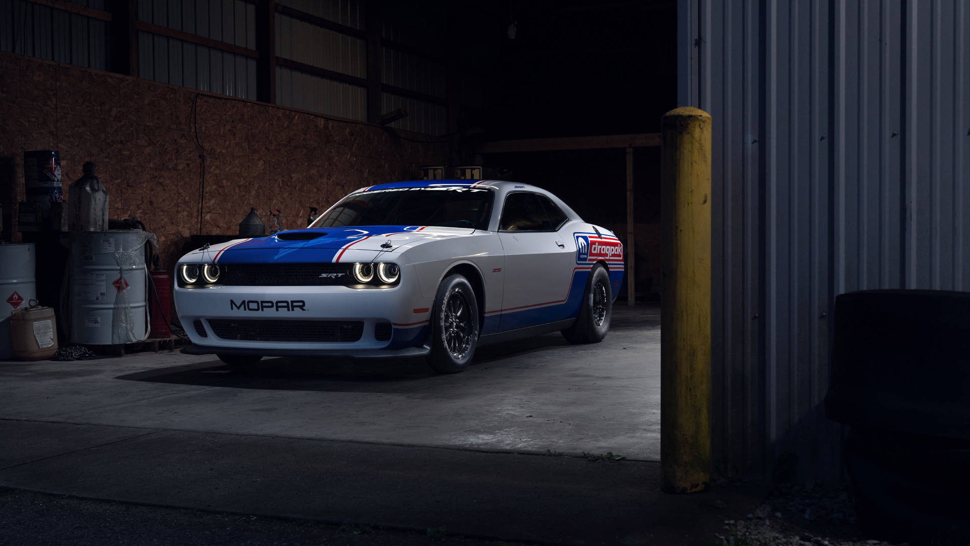 跑車 桌布 壁紙 — 一輛白色、藍色和紅色的Mopar Dodge Challenger賽車停放在光線昏暗的車庫中，旁邊有工業用桶和黃色柱子。