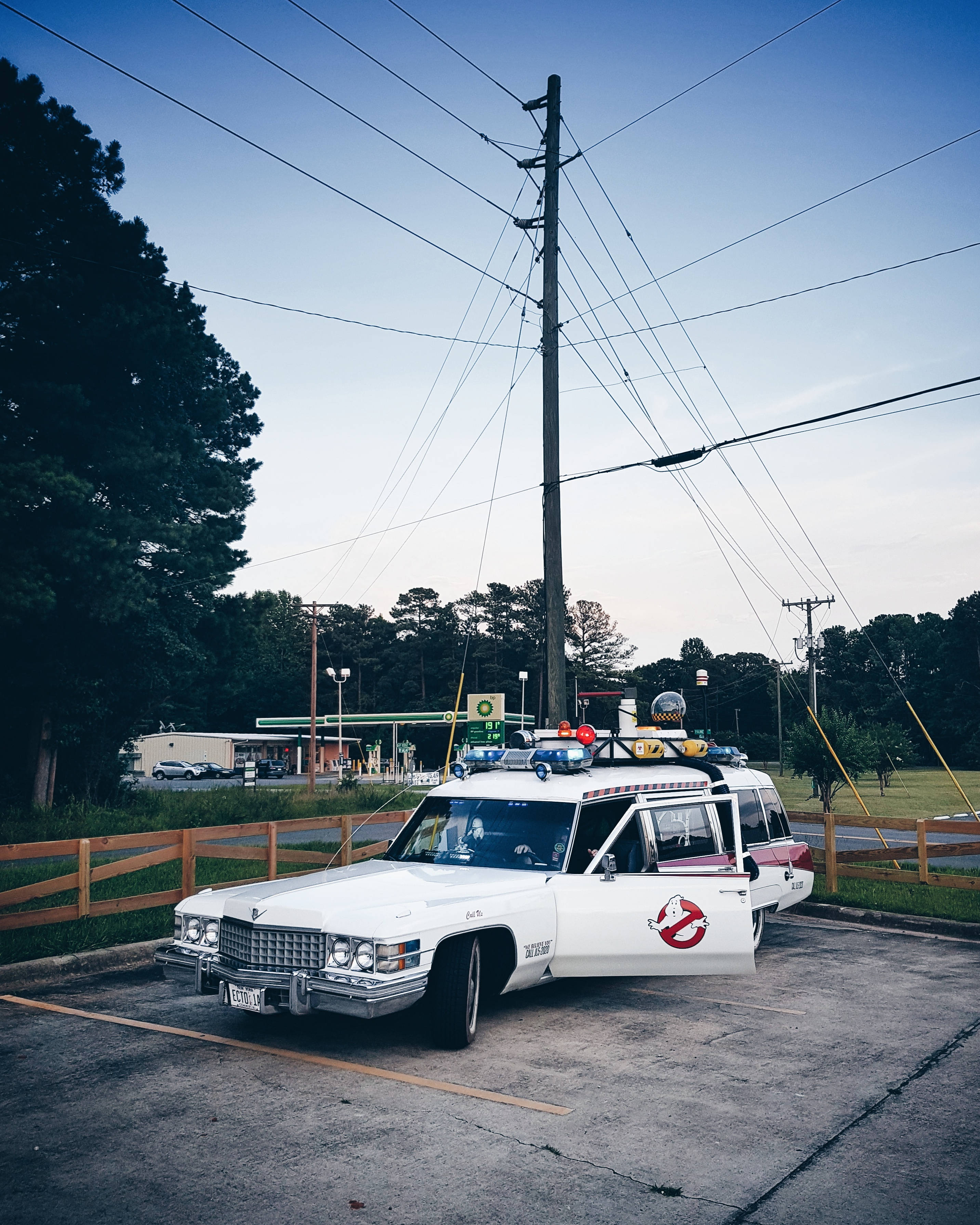 Ghostbusters 桌布 壁紙 — 一輛白色1980年代凱迪拉克靈車，帶有魔鬼剋星標誌和裝備，在黃昏時停放在路邊停車場。