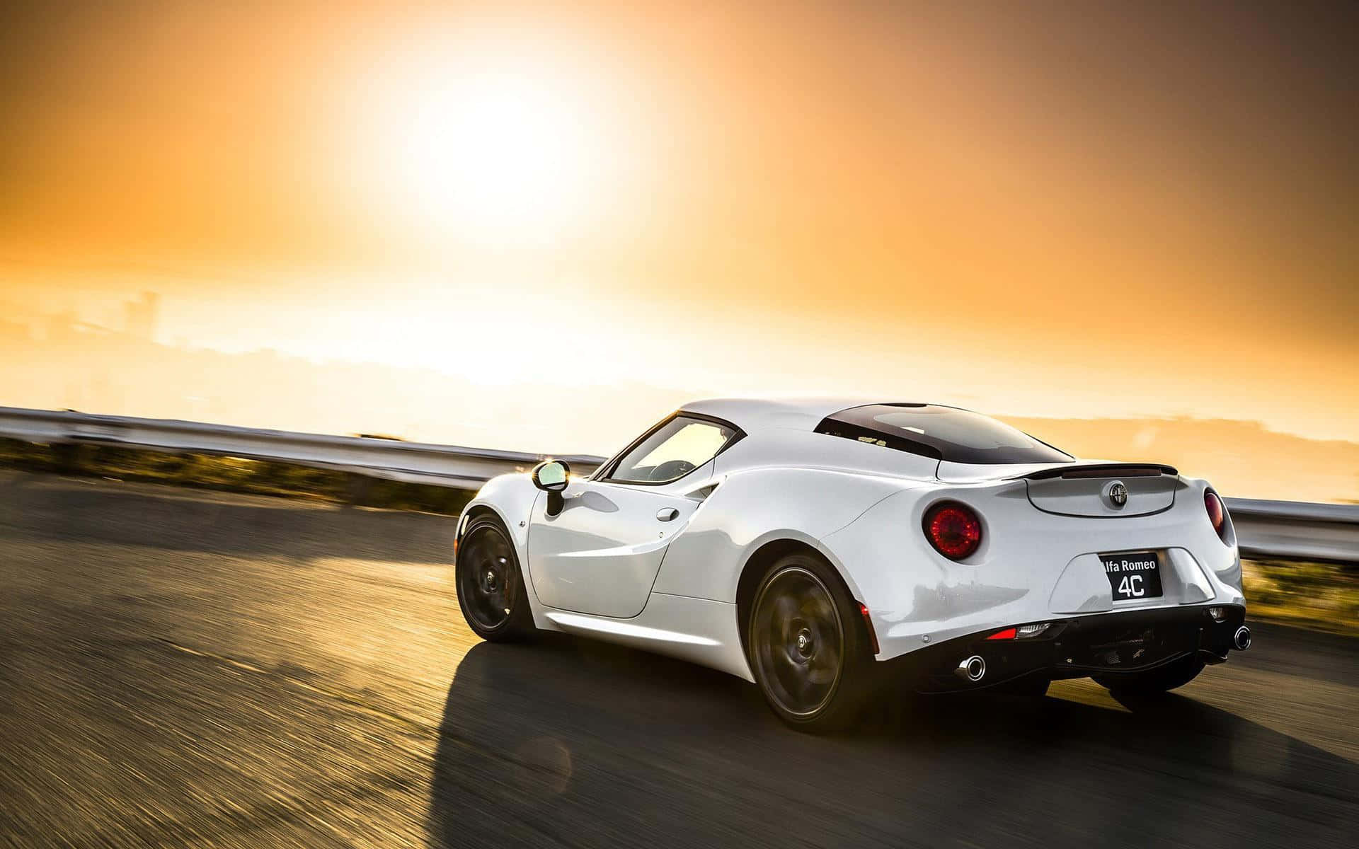 Alfa Romeo 4c 桌布 壁紙 — 一輛白色Alfa Romeo 4C跑車在日落時分沿著海岸公路奔馳，金色光芒劃過路面。