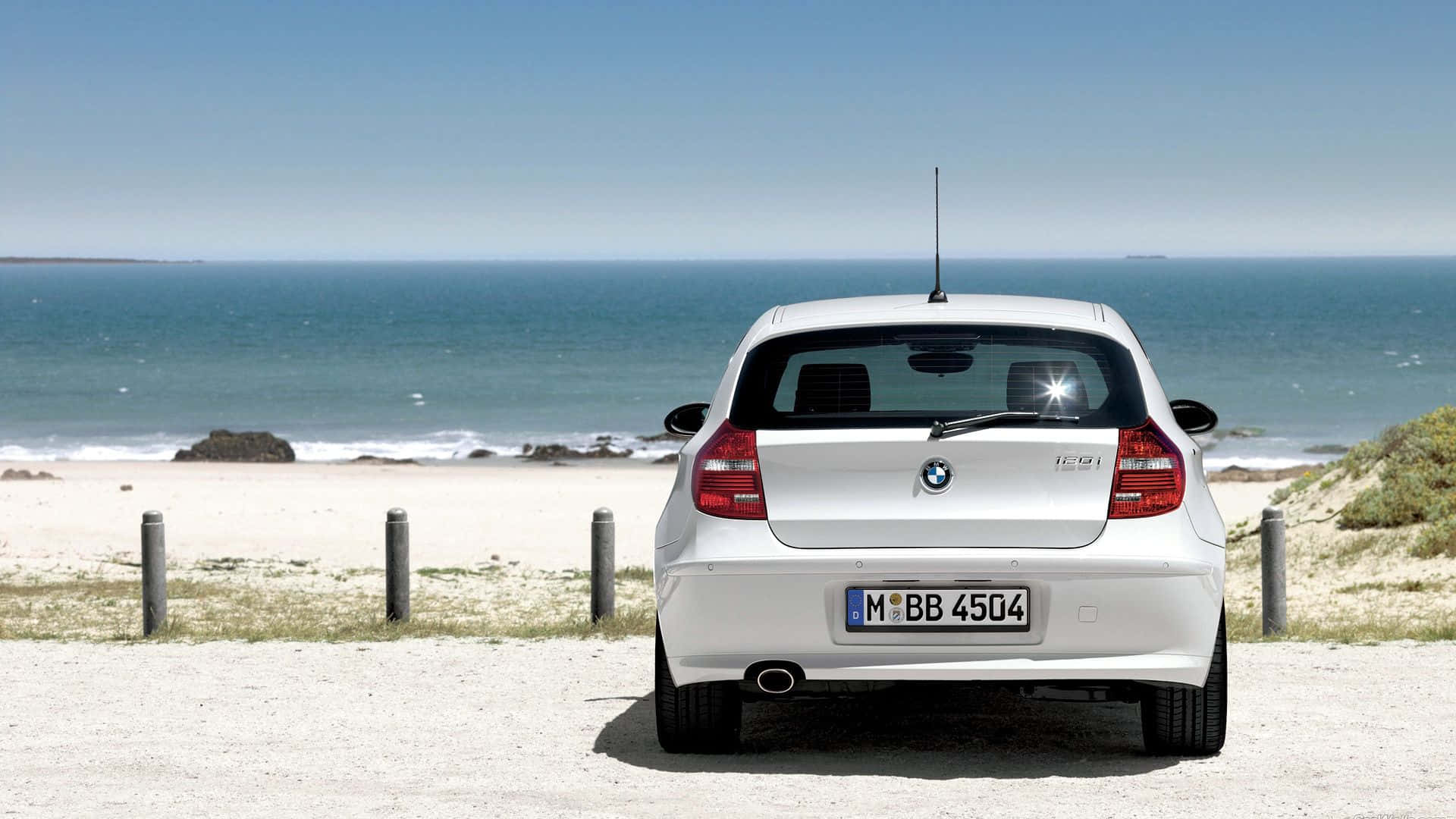 Bmw 1 Series 桌布 壁紙 — 一輛白色BMW 1系列停泊在碎石路上，面向晴朗天空下廣闊的藍色海洋。