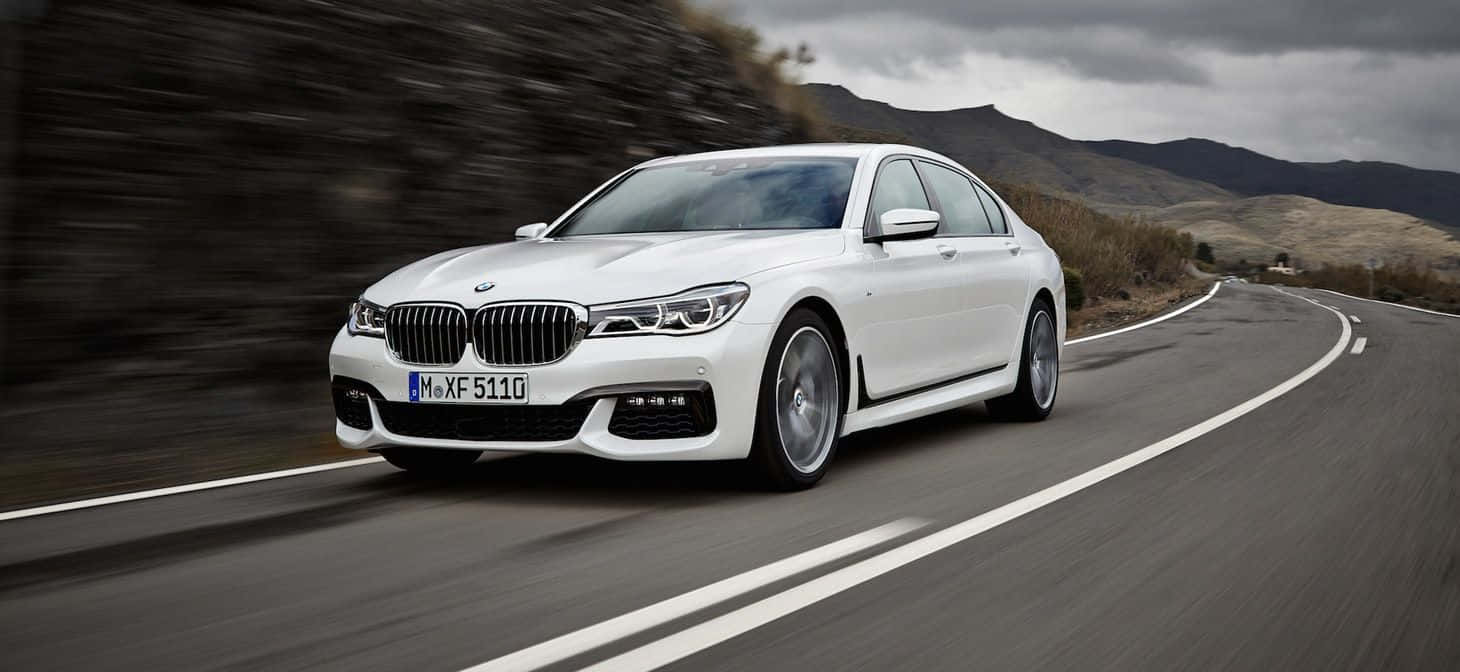 Bmw 7 Series 桌布 壁紙 — 一輛白色BMW 7系列轎車在多雲的天空下沿著蜿蜒的山路疾馳。