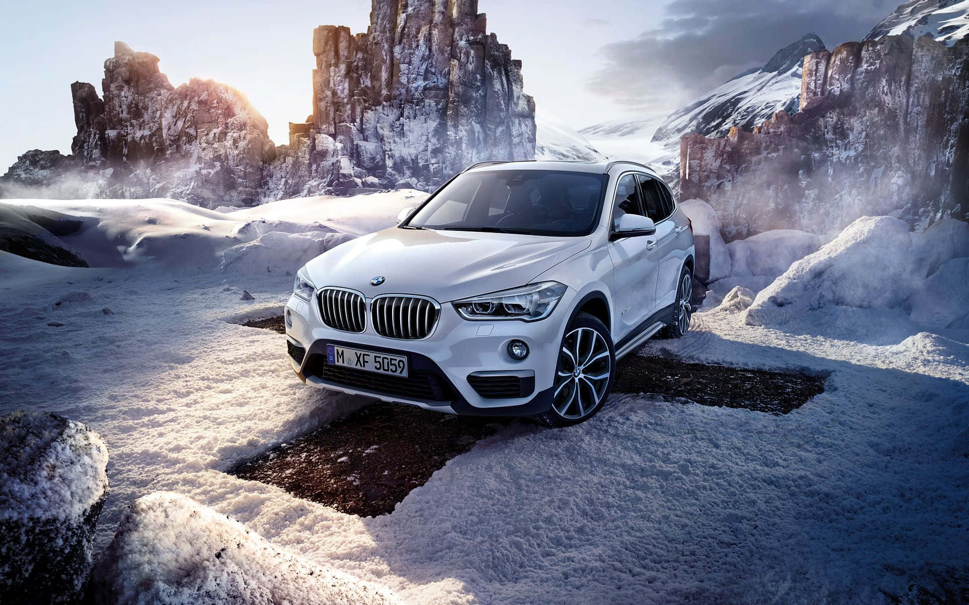 Bmw X1 桌布 壁紙 — 一輛白色BMW SUV停在積雪的山口，背景是崎嶇的懸崖和陽光照耀的山峰。