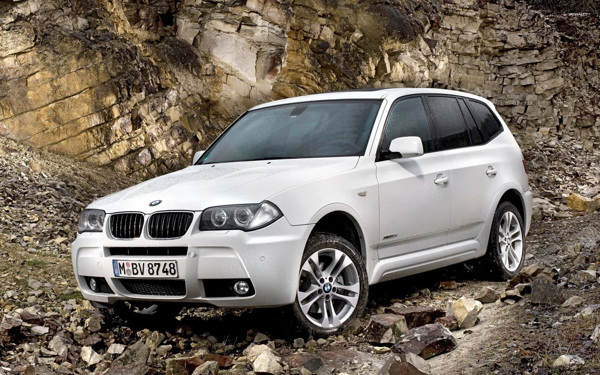 Bmw X3 桌布 壁紙 — 一輛白色BMW SUV在崎嶇岩石地形上行駛，旁邊是風化的石崖。