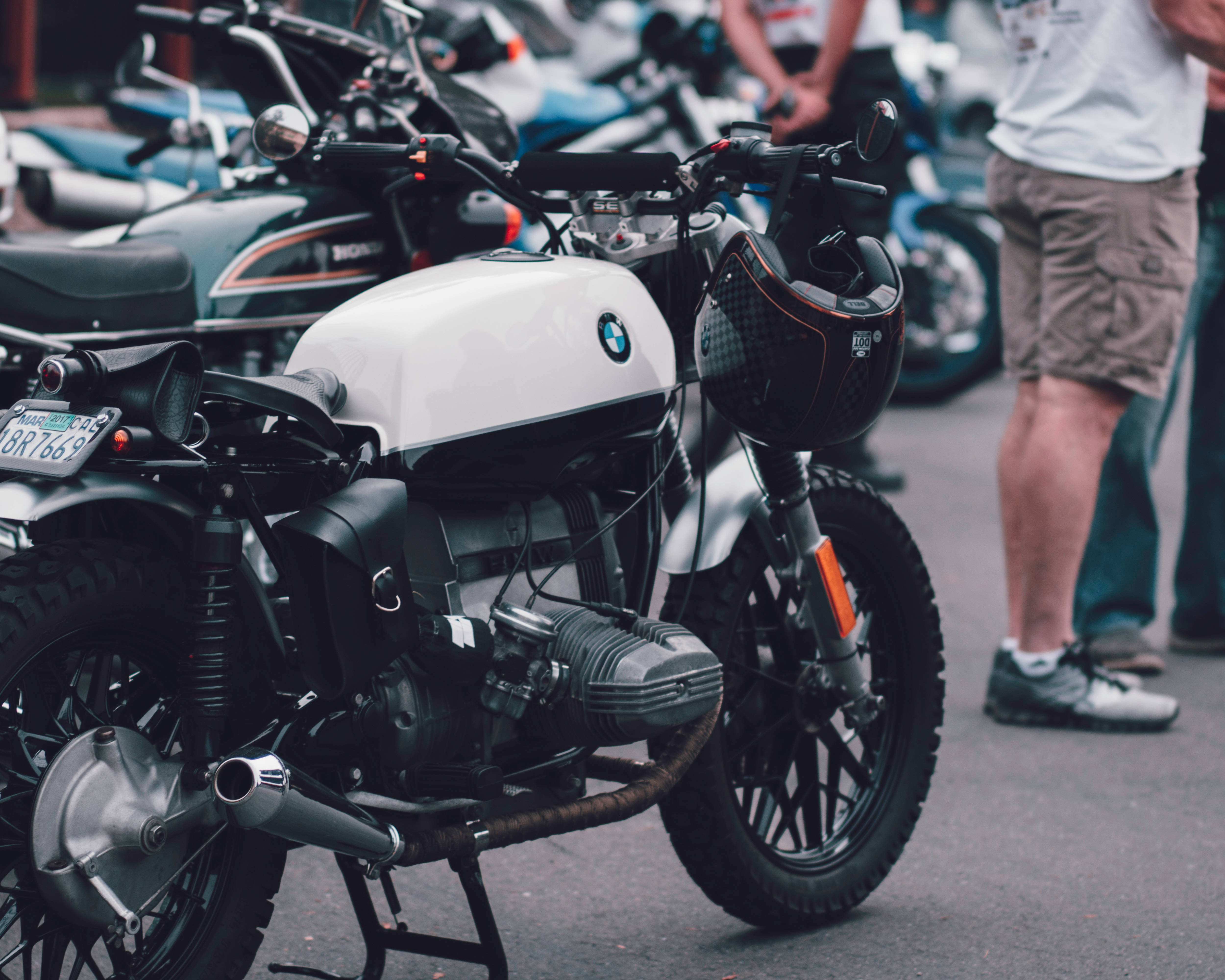 機車 桌布 壁紙 — 一輛白色BMW摩托車，黑色安全帽掛在把手上，與其他摩托車一起停放在街上。