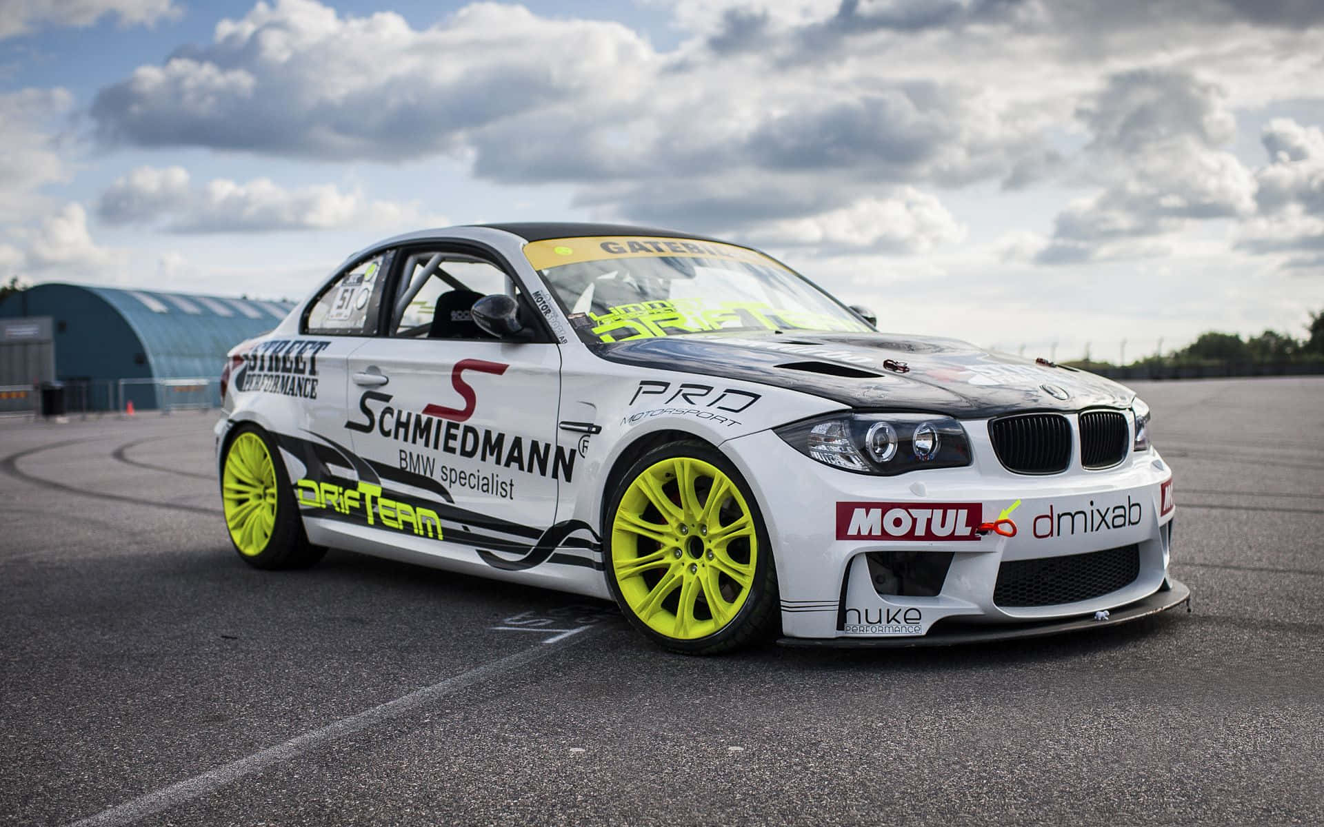 Bmw 1 Series 桌布 壁紙 — 一輛白色BMW甩尾車配備螢光黃色輪胎，在多雲的天空下於瀝青賽道上奔馳。