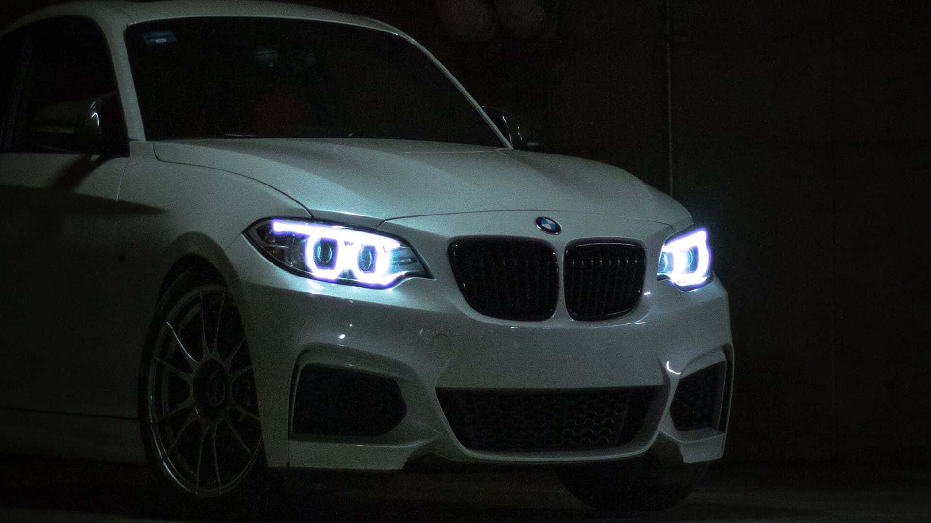 黑色 桌布 壁紙 — 一輛白色BMW跑車在黑暗的車庫中發出明亮車頭燈的光芒，在其光滑表面投射出銳利的反射。
