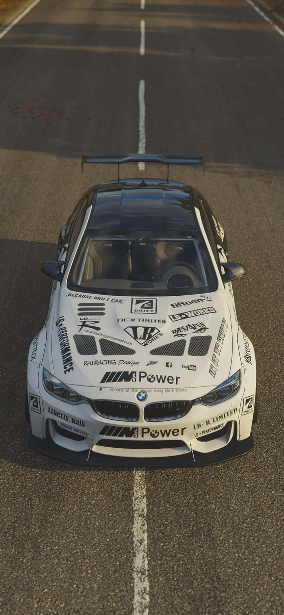 iPhone Xs Forza Horizon 4 桌布 壁紙 — 一輛白色BMW飄移賽車，車身佈滿贊助商標誌，停放在一條有白色標線的瀝青賽道中央。
