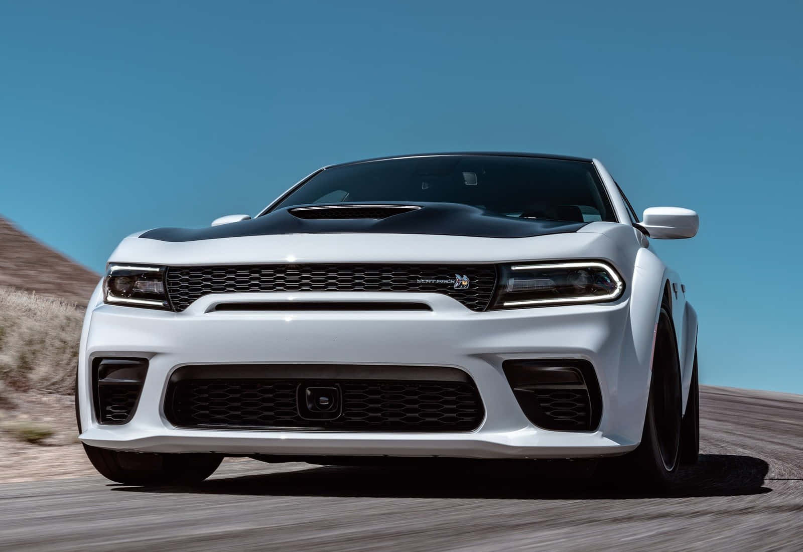 Scat Pack 桌布 壁紙 — 一輛白色Dodge Challenger Hellcat帶有黑色引擎蓋條紋，在晴朗藍天下沿沙漠公路疾馳。
