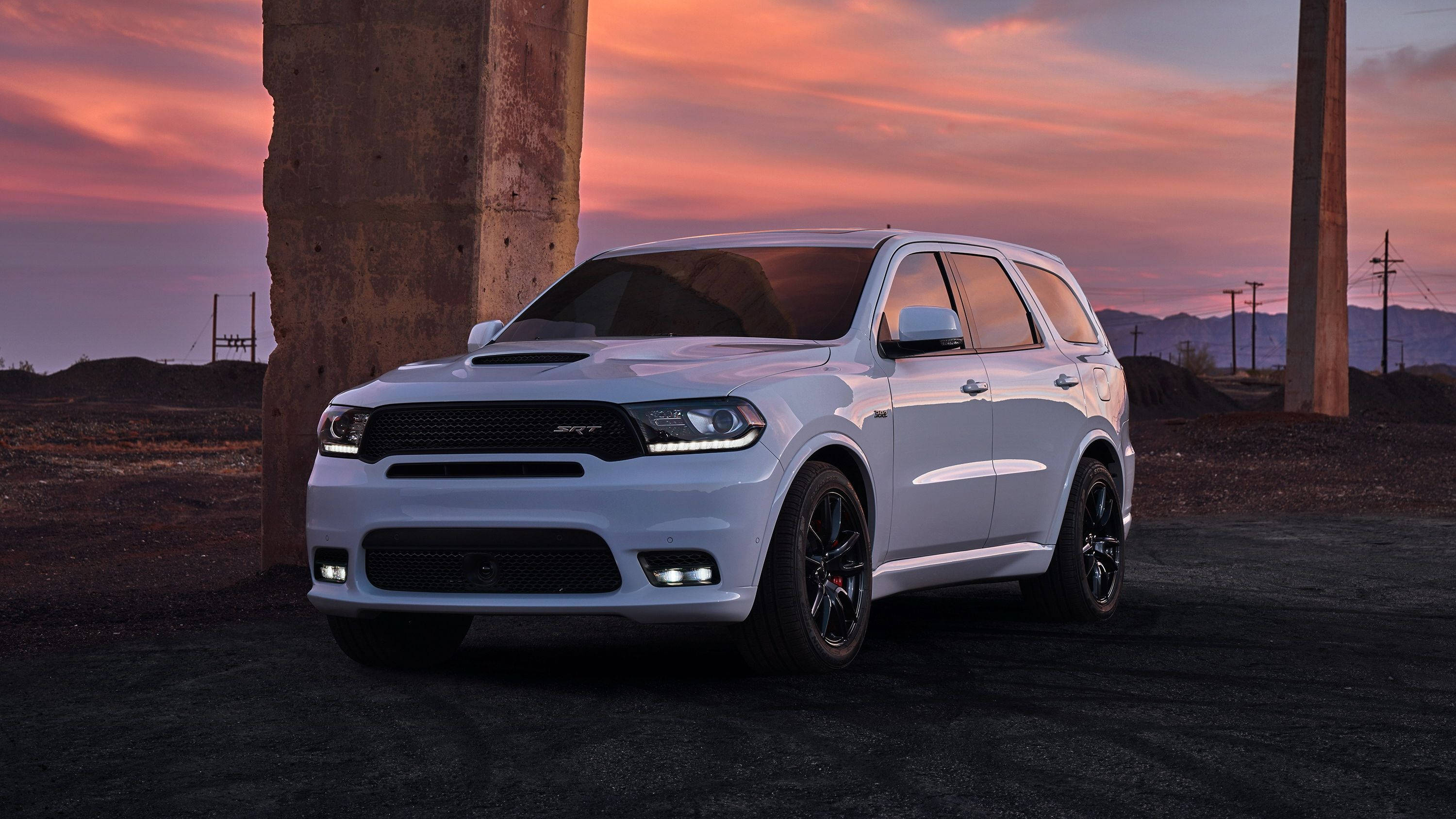 Dodge 桌布 壁紙 — 一輛白色Dodge Durango SRT SUV停放在混凝土柱下，背景是戲劇性的粉紅和橙色日落。