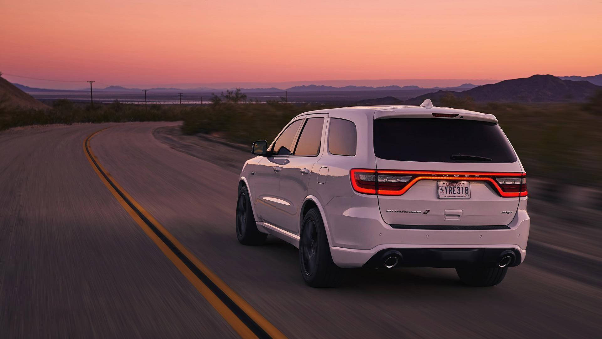 Dodge 桌布 壁紙 — 一輛白色Dodge Durango SUV在日落時分沿沙漠高速公路飛馳，天空呈現粉紅色和橙色。