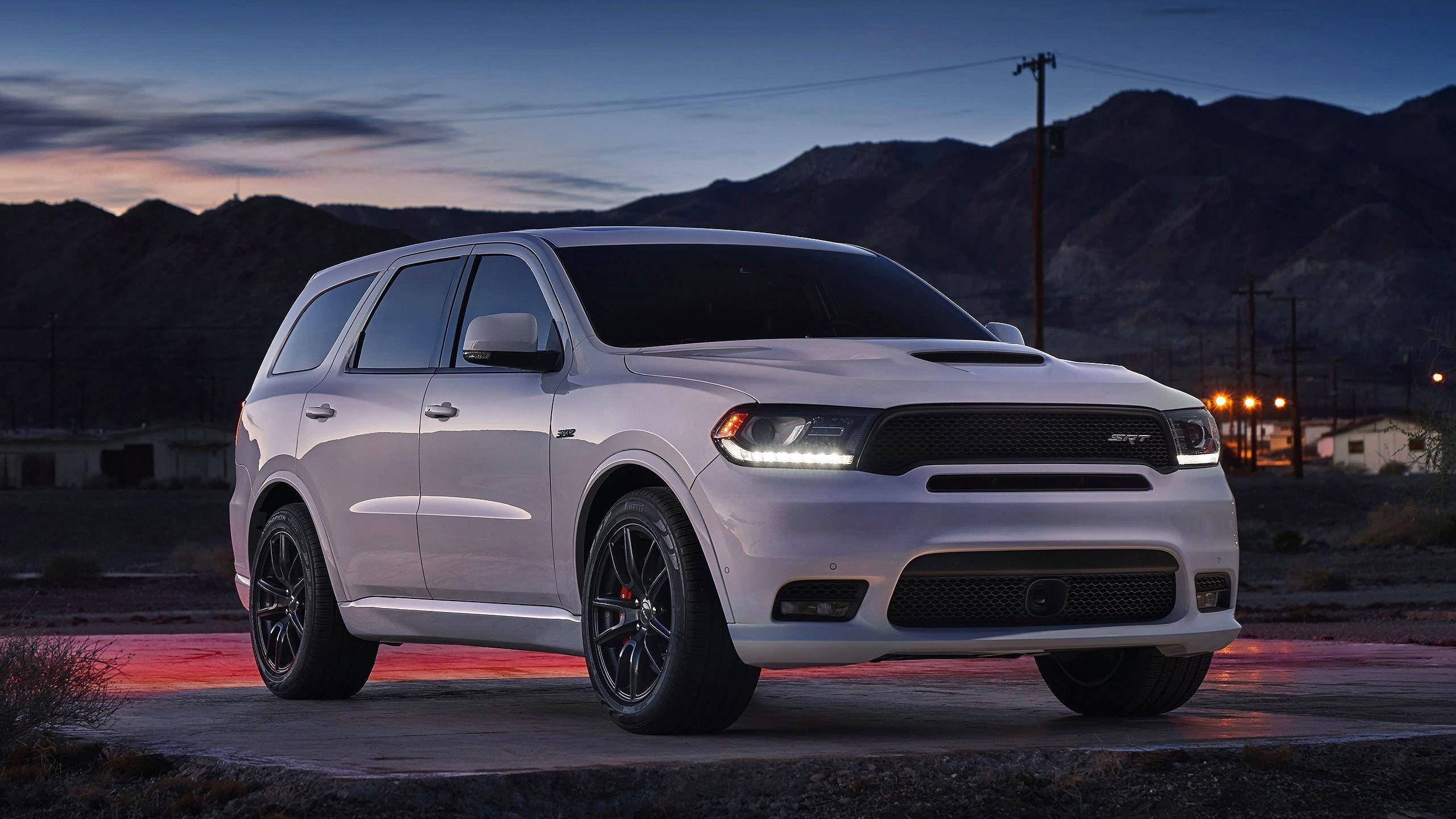 Dodge 桌布 壁紙 — 一輛白色Dodge Durango SRT SUV，配黑色輪圈，停泊在黃昏時分的混凝土墊上，背景有山脈和遠處燈光。