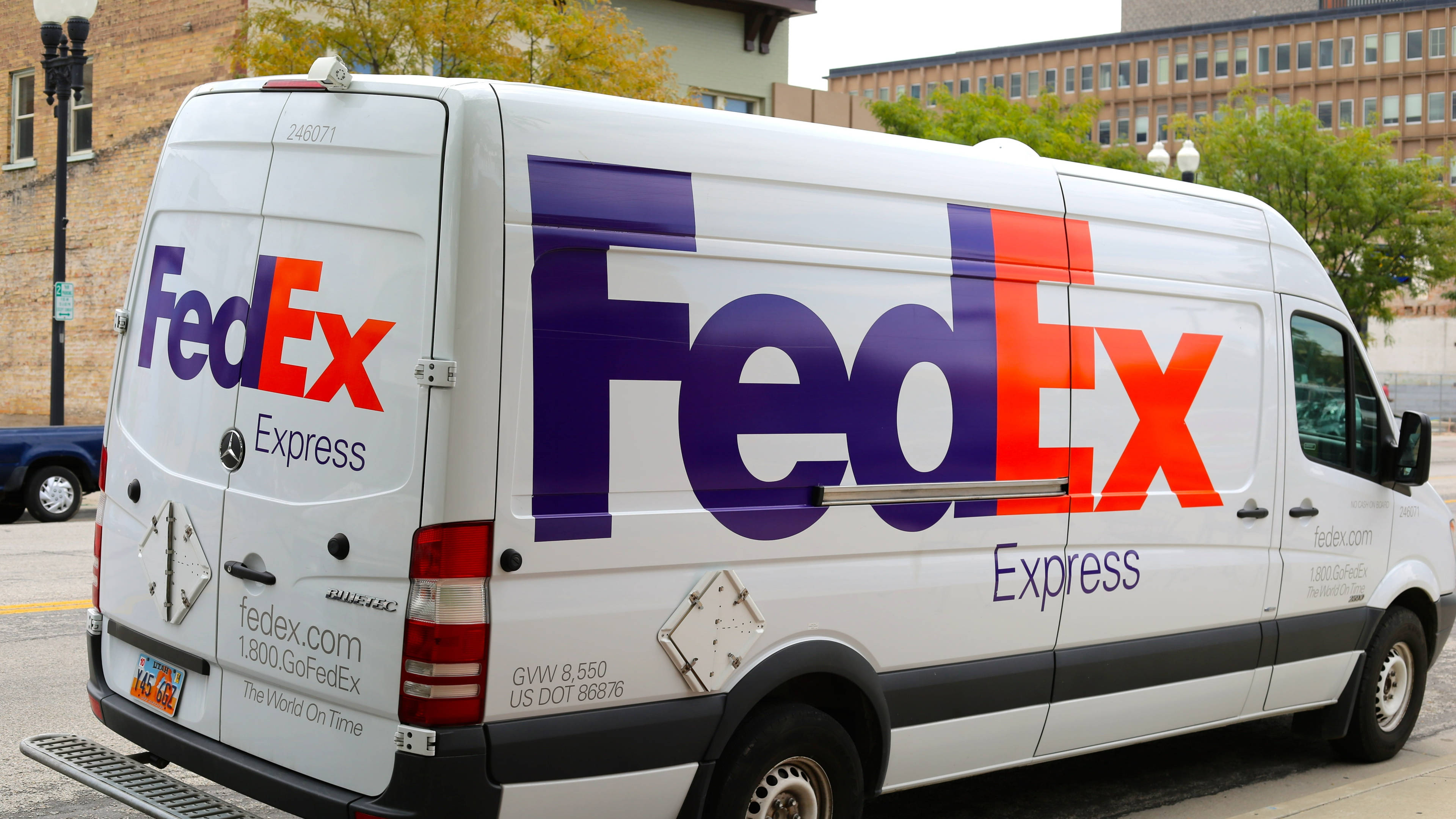 聯邦快遞 桌布 壁紙 — 一輛白色FedEx Express送貨車停放在城市街道上，背景有建築物和樹木。
