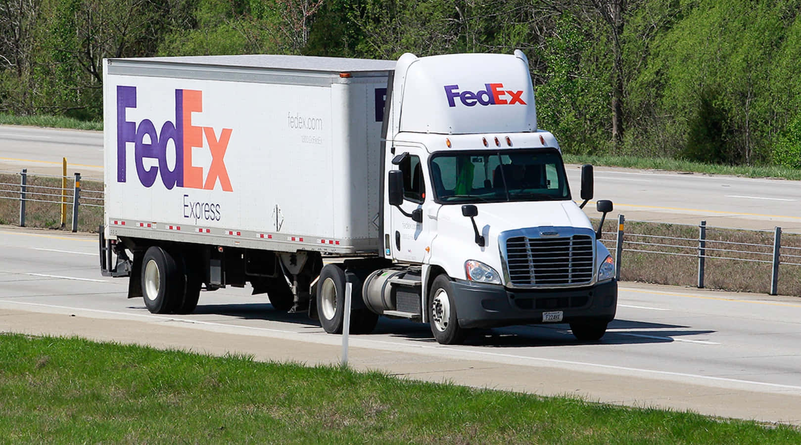 聯邦快遞 桌布 壁紙 — 一輛白色FedEx Express半掛卡車在陽光明媚的高速公路上行駛，兩旁綠樹成蔭，草地青翠。