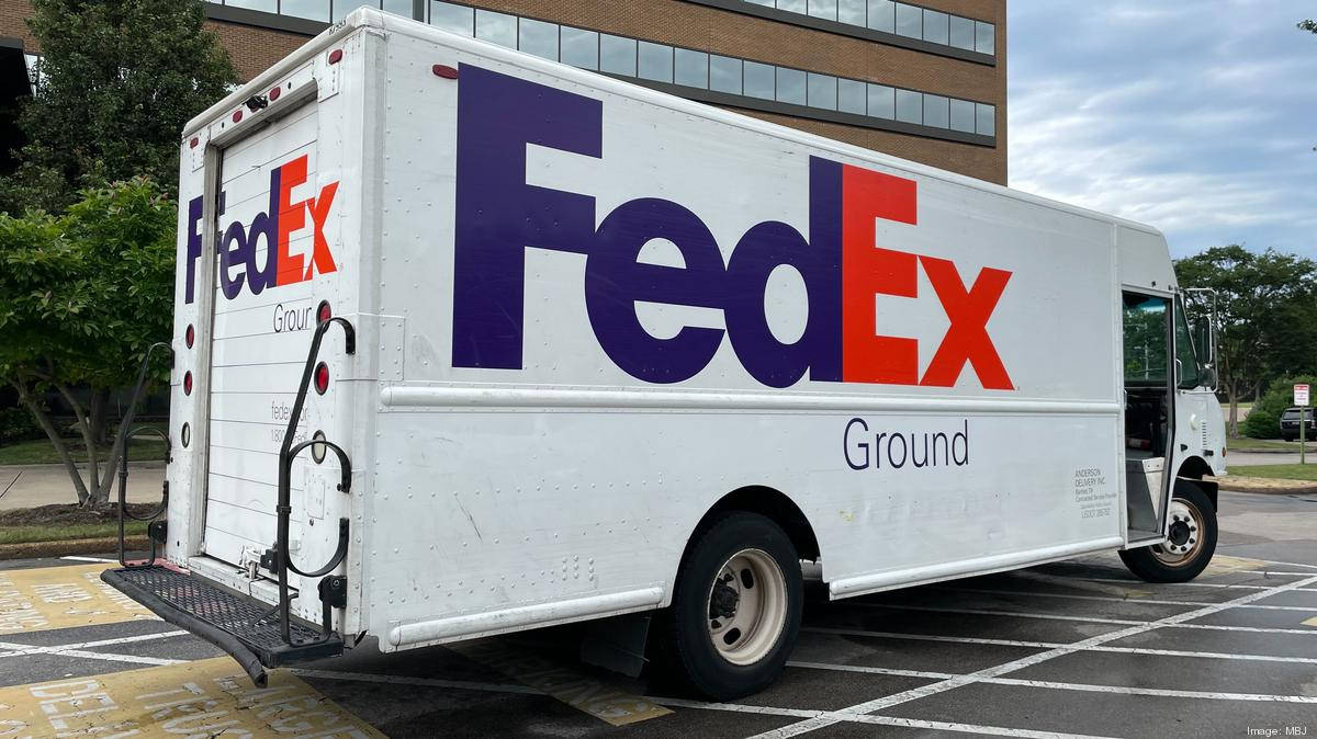 聯邦快遞 桌布 壁紙 — 一輛白色FedEx Ground送貨車停在停車場，背景有樹木和磚造建築，天空多雲。