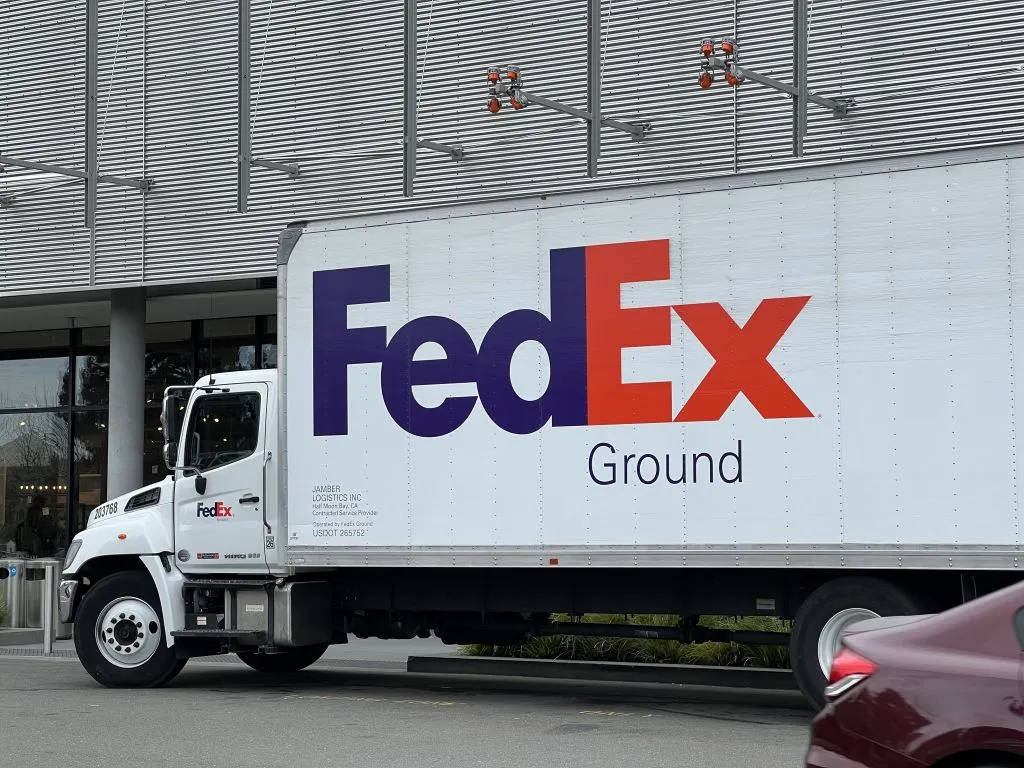 聯邦快遞 桌布 壁紙 — 一輛白色FedEx Ground卡車停放在現代建築外，建築物有波紋金屬牆板和玻璃窗。