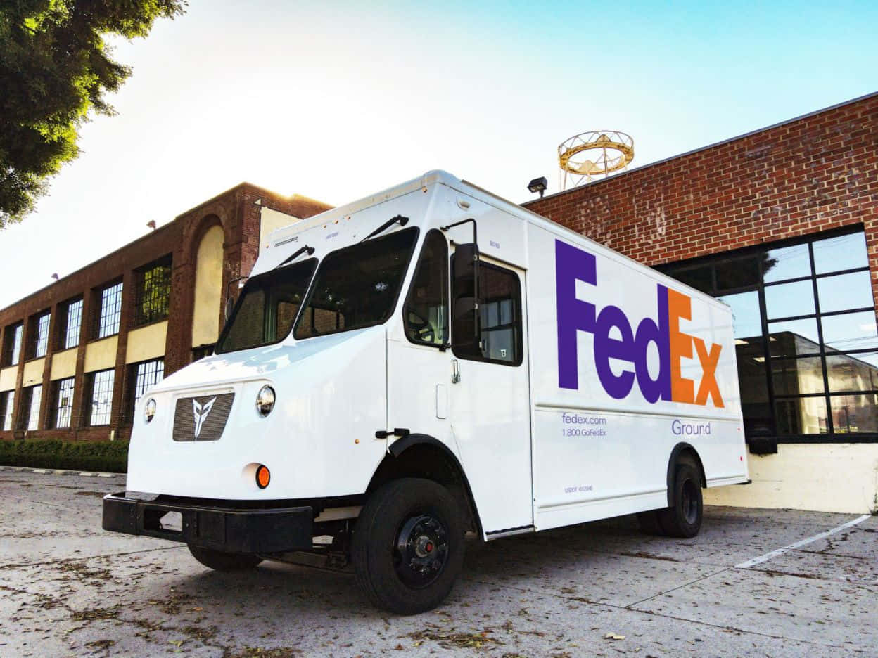 聯邦快遞 桌布 壁紙 — 一輛白色FedEx Ground送貨車停在磚砌建築前，天空清澈湛藍。