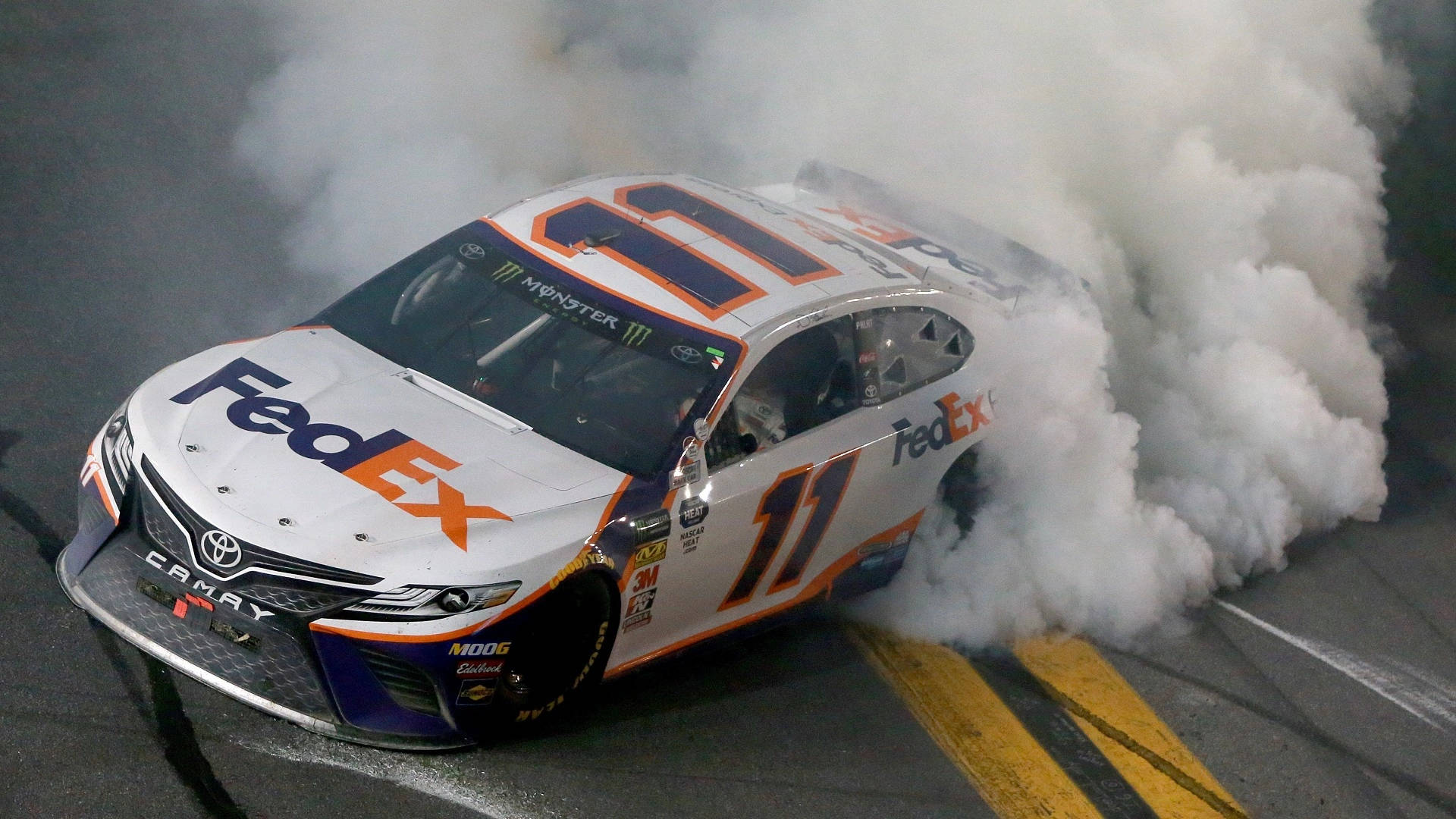 Denny Hamlin 桌布 壁紙 — 一輛白色FedEx Toyota Camry賽車（號碼11）在夜間賽道上進行戲劇性的燒胎，冒出濃煙。