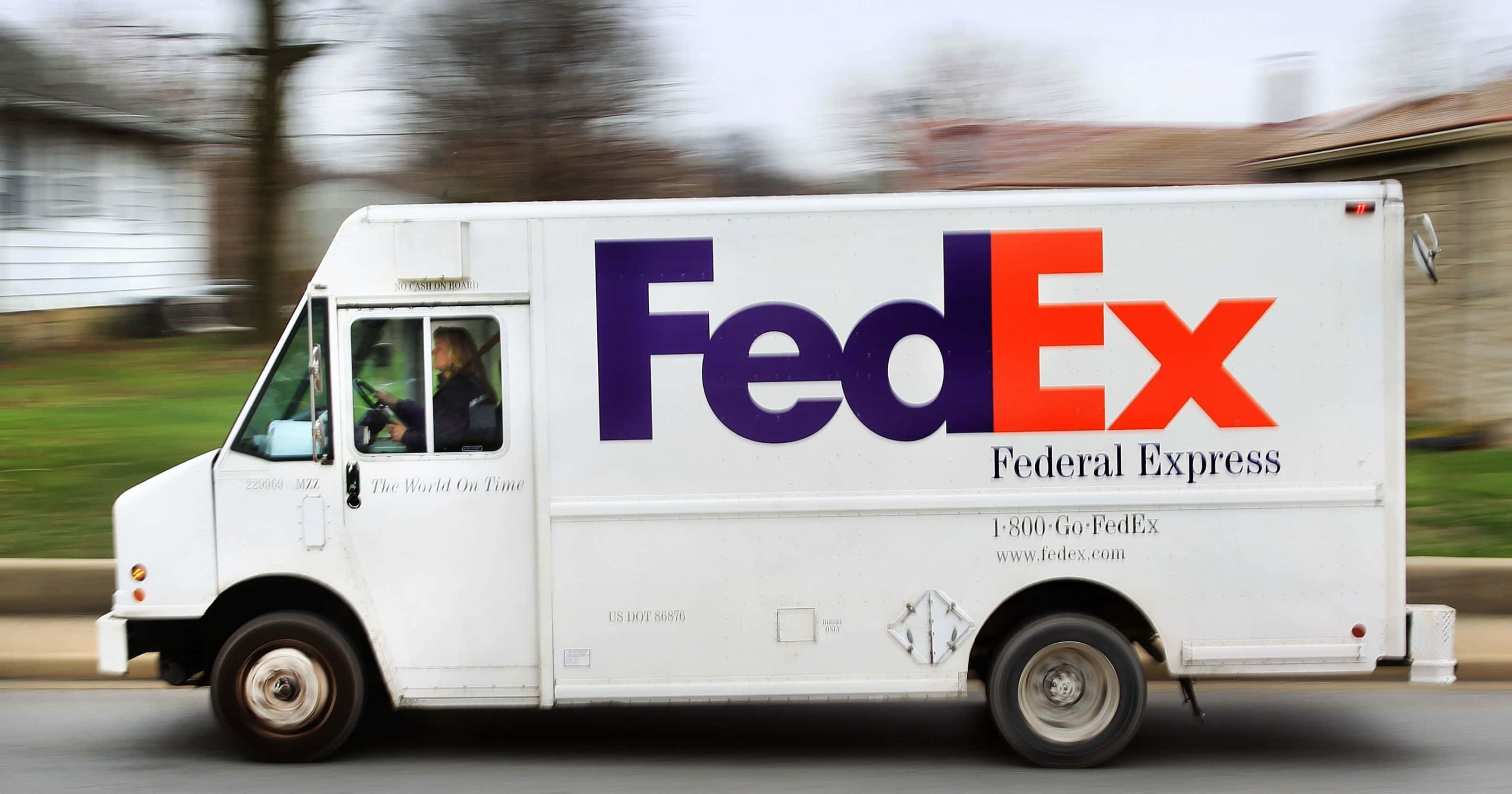聯邦快遞 桌布 壁紙 — 一輛白色FedEx送貨車在郊區道路上疾馳，背景有模糊的樹木和房屋。