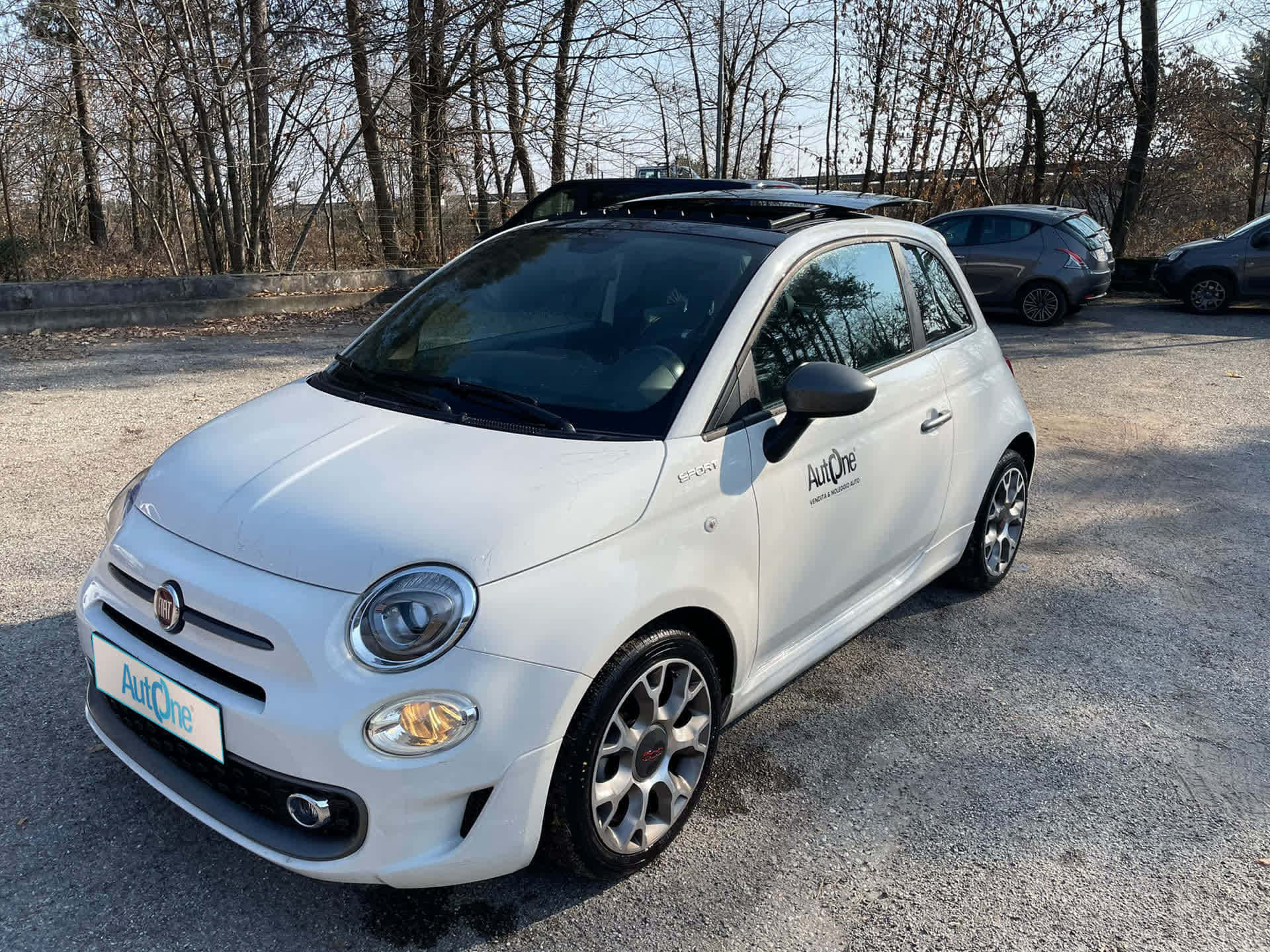 Fiat 桌布 壁紙 — 一輛白色Fiat 500停在碎石上，背景有光禿禿的樹木，在晴朗的日光下。