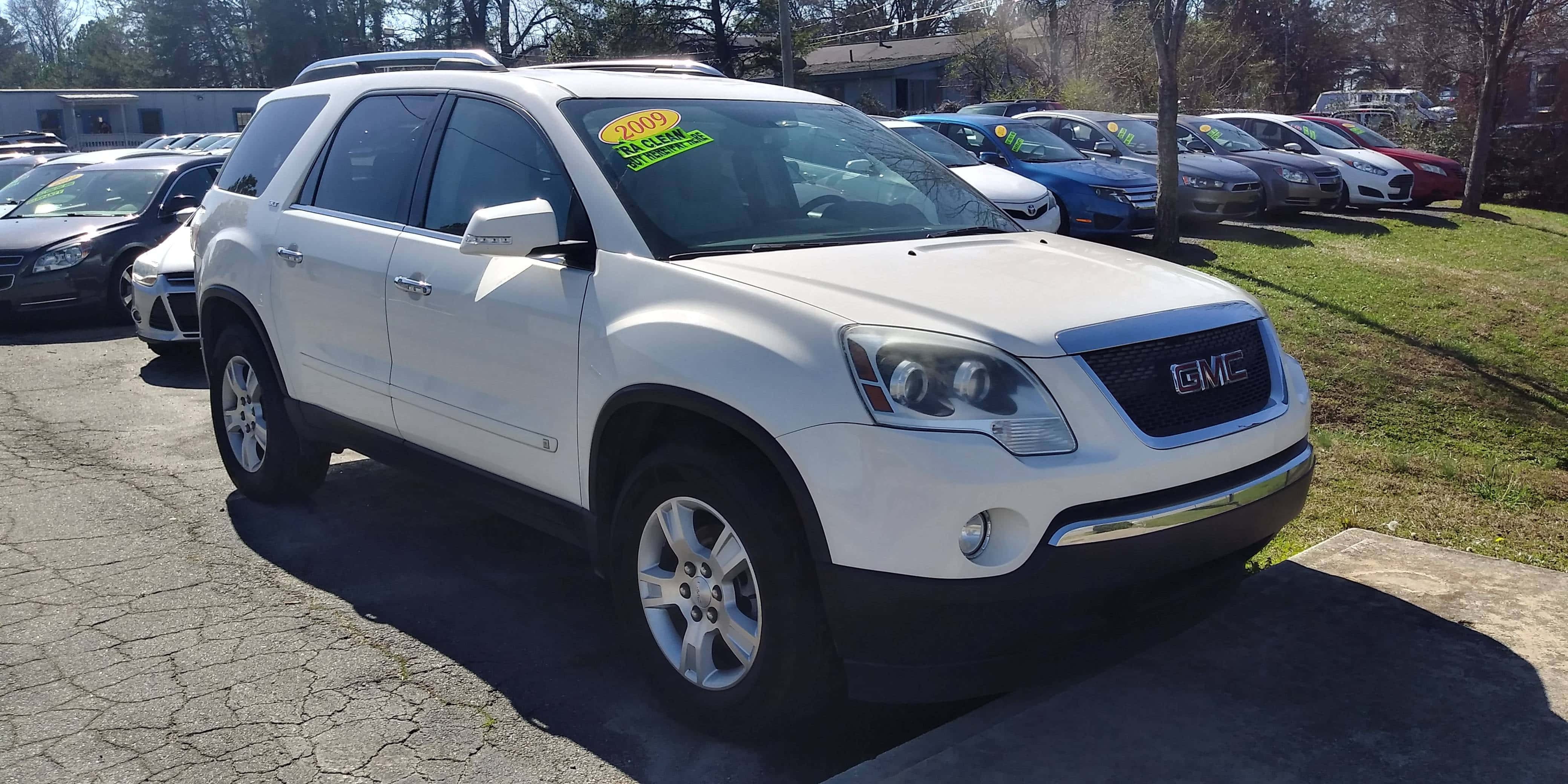 Gmc Acadia 桌布 壁紙 — 一輛白色GMC Acadia SUV停放在陽光明媚的停車場，背景有其他汽車和樹木。