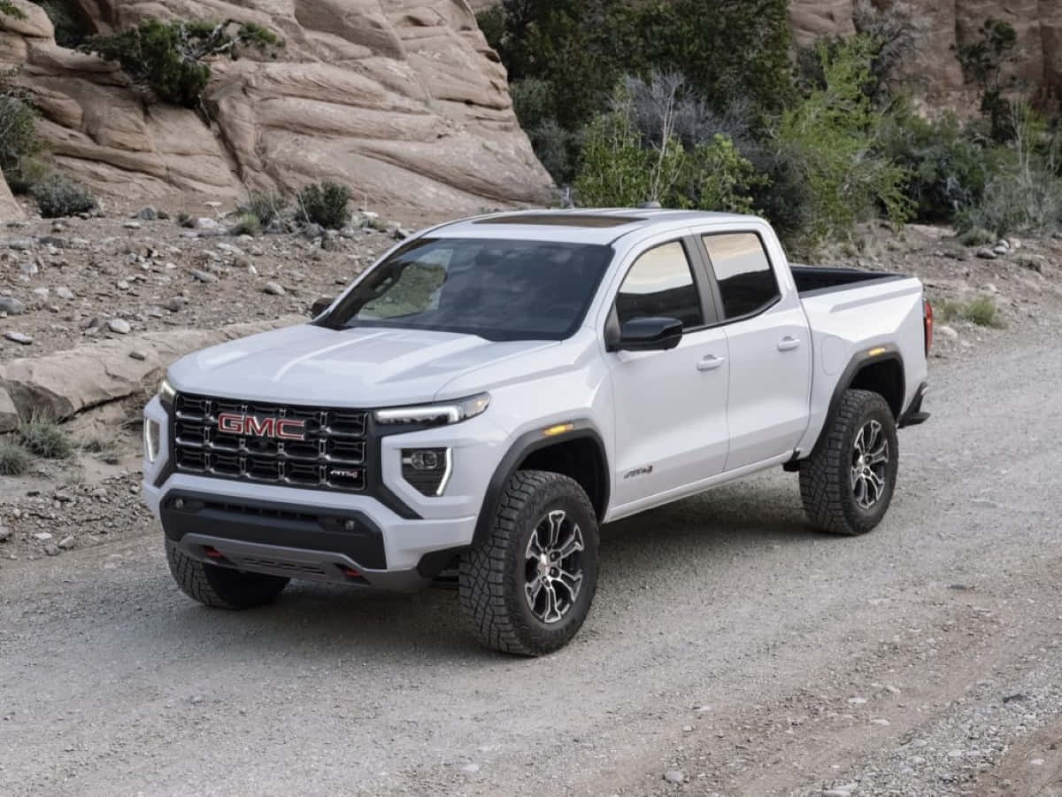 Gmc Canyon 桌布 壁紙 — 一輛白色GMC Canyon AT4皮卡車停在碎石路上，旁邊是岩石沙漠地形，植被稀疏。