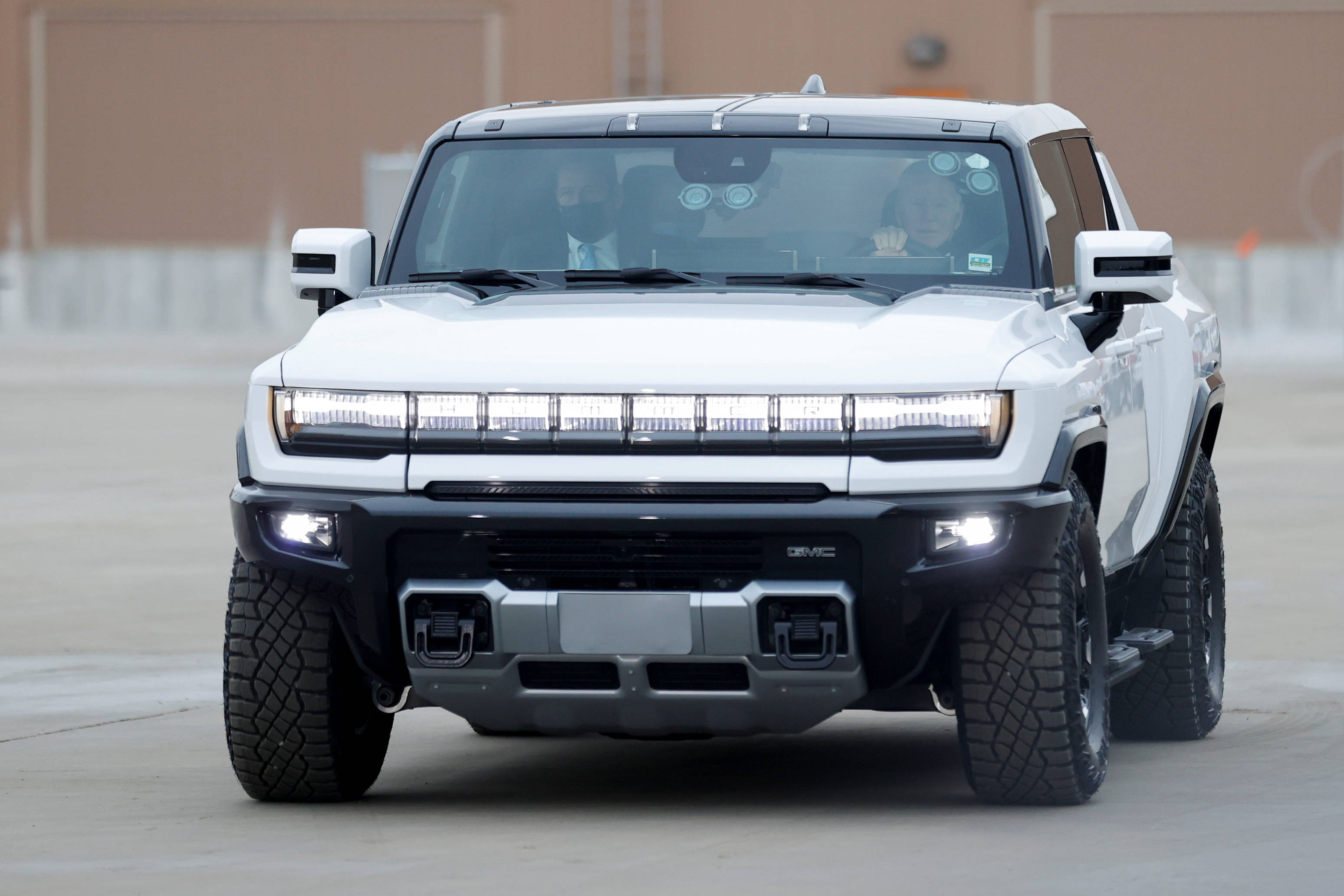 Truck 桌布 壁紙 — 一輛白色GMC Hummer EV SUV，配備堅固輪胎和發光頭燈，在混凝土表面上向前方。