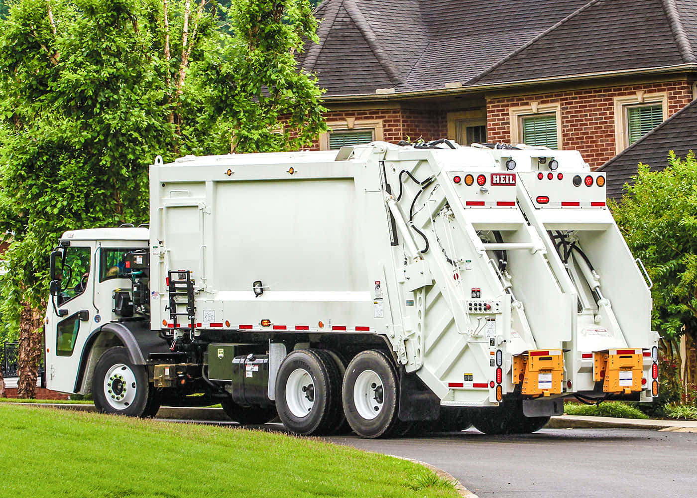Garbage Truck 桌布 壁紙 — 一輛白色Heil垃圾車停泊在郊區街道上，旁邊是磚屋和綠色草坪。