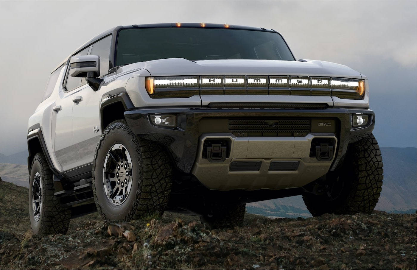 Truck 桌布 壁紙 — 一輛白色Hummer EV SUV大膽地矗立在岩石山坡上，遠山在陰天背景下若隱若現。