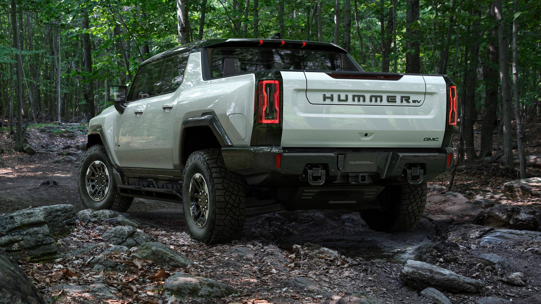 Truck 桌布 壁紙 — 一輛白色Hummer EV卡車在岩石森林小徑上行駛，周圍環繞著高大的綠色樹木。