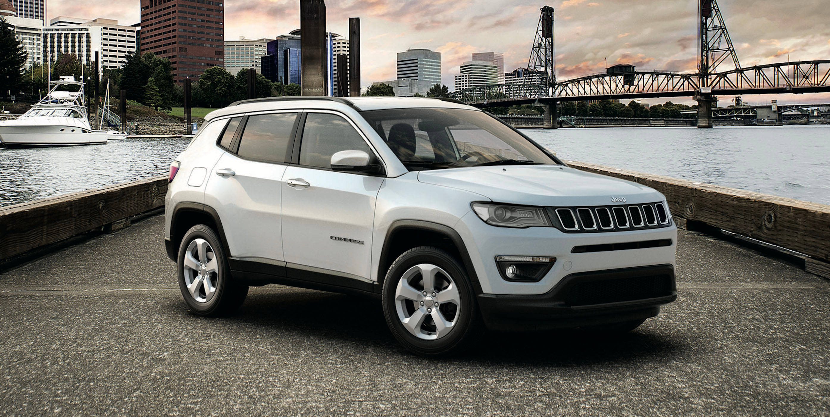 汽車 桌布 壁紙 — 一輛白色Jeep Compass停泊在海濱碼頭，背景是日落時分的城市天際線和橋樑。