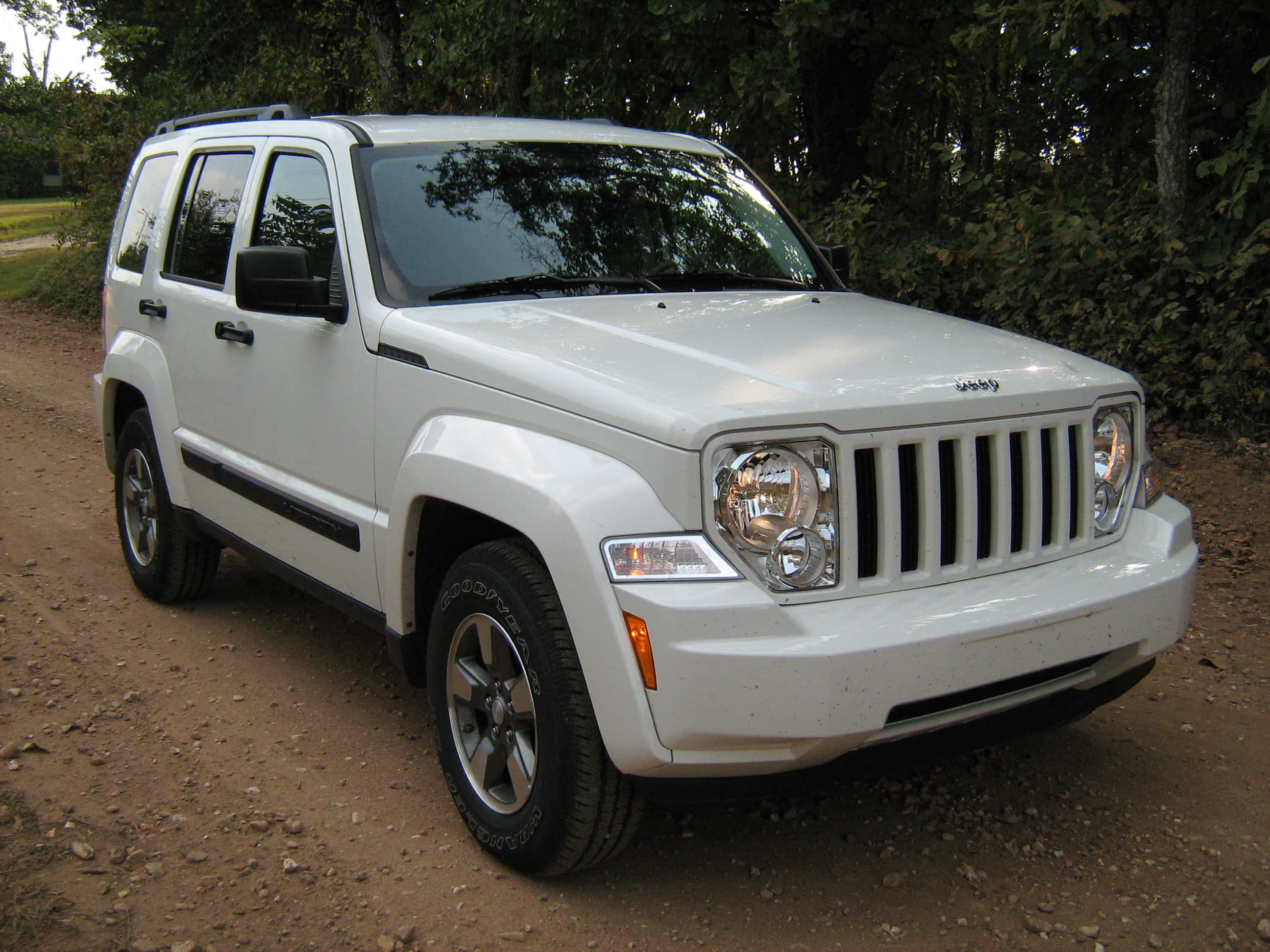 Jeep Liberty 桌布 壁紙 — 一輛白色Jeep Liberty SUV停放在被茂密綠樹環繞的泥土路上。