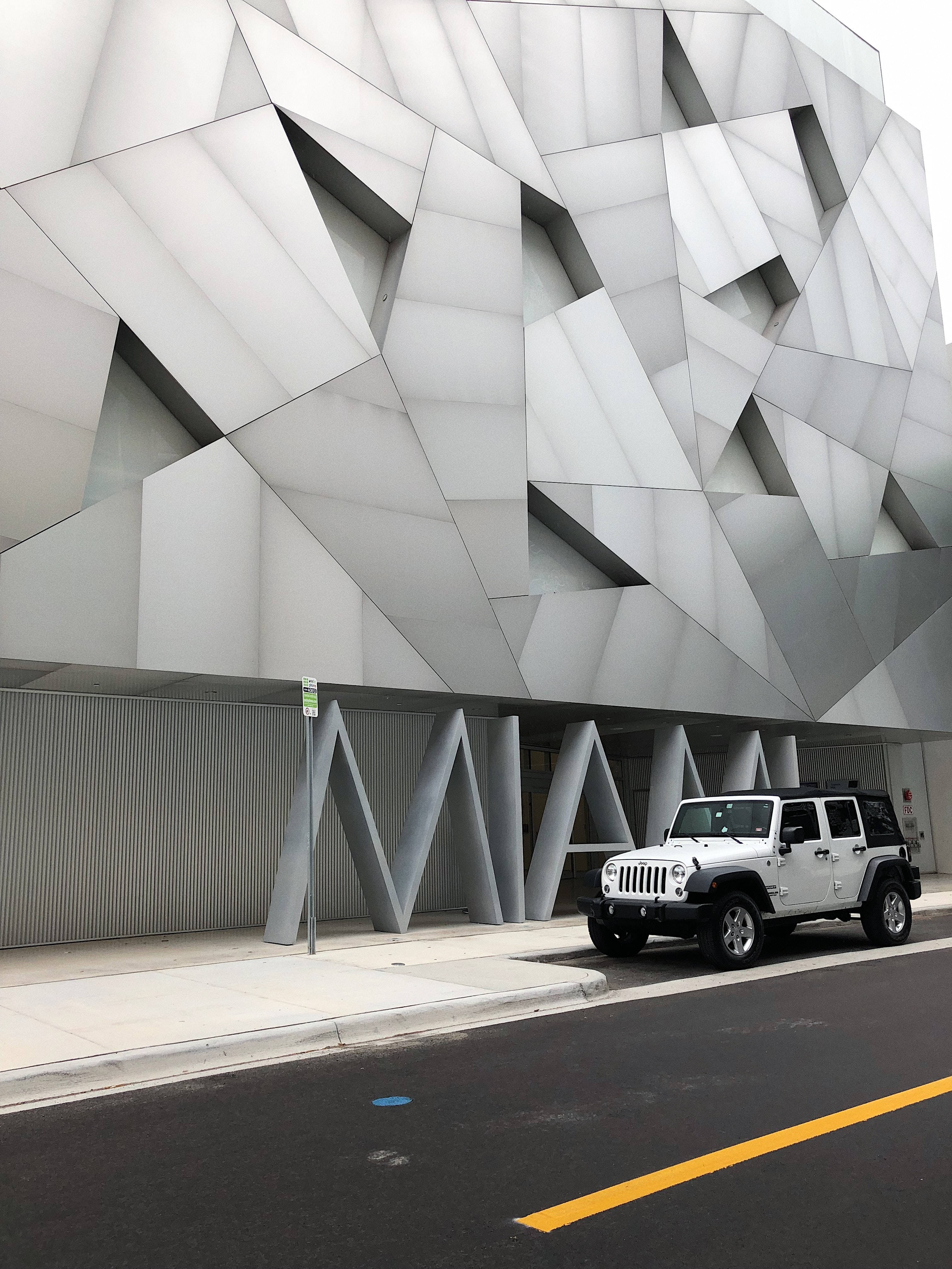 吉普 桌布 壁紙 — 一輛白色Jeep Wrangler停在一條街道上，前面是一座引人注目的現代建築，帶有棱角分明的白色金屬面板。