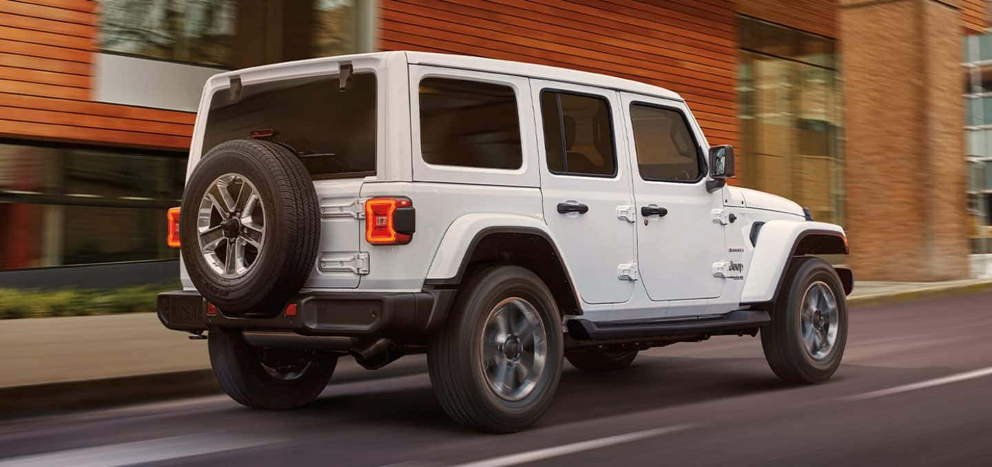 吉普 桌布 壁紙 — 一輛白色Jeep Wrangler在街上以動態模糊駛過一座現代磚砌建築。