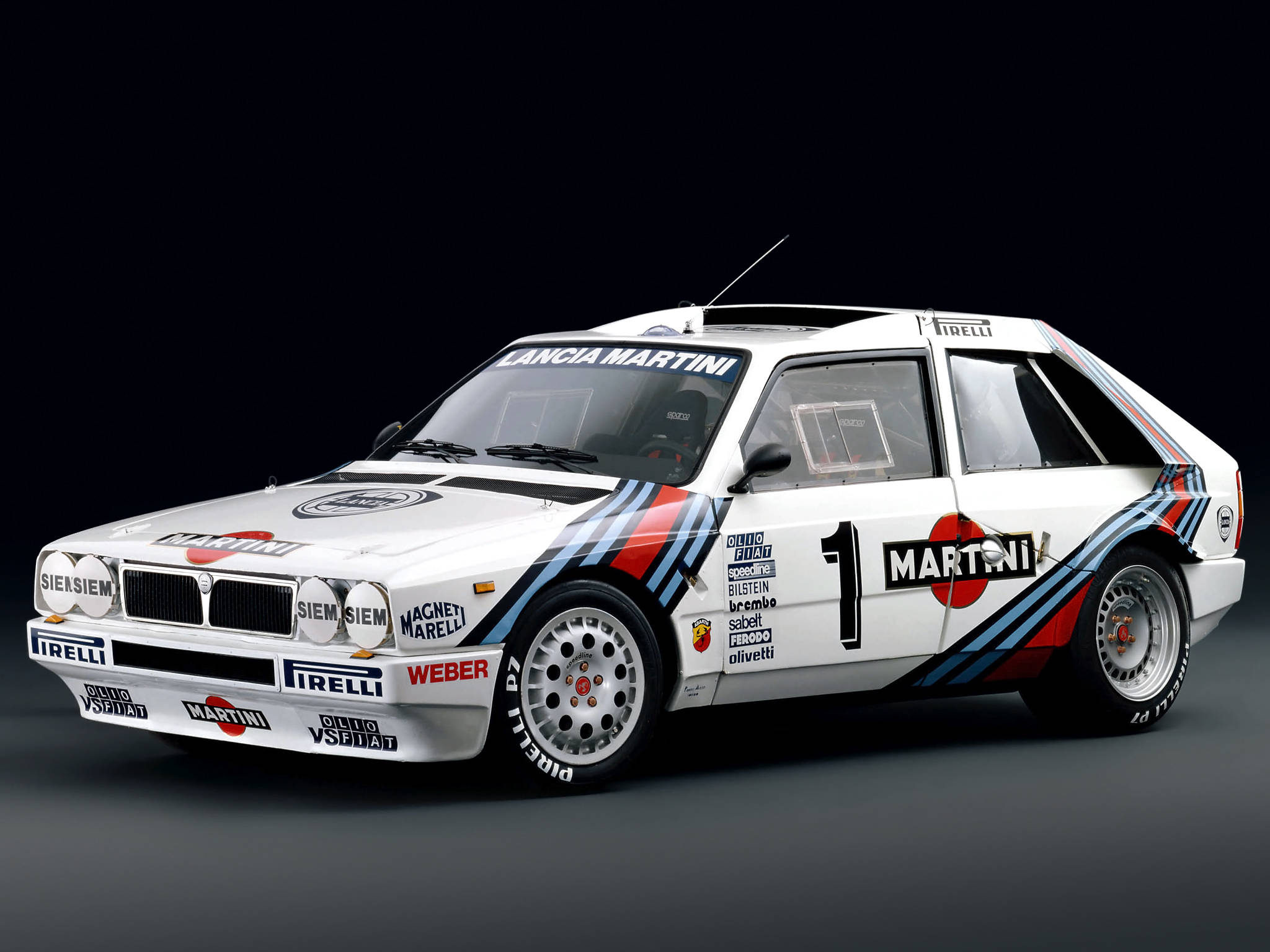 rally 桌布 壁紙 — 一輛白色Lancia Delta S4拉力賽車，帶有Martini塗裝和1號車號，在深色攝影棚背景下蓄勢待發。