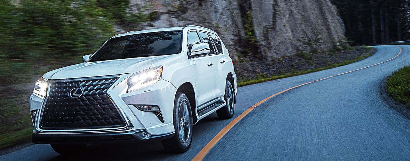 Lexus Gx 460 桌布 壁紙 — 一輛白色Lexus SUV沿著蜿蜒的山路疾駛，背景是模糊的綠樹和岩石峭壁。