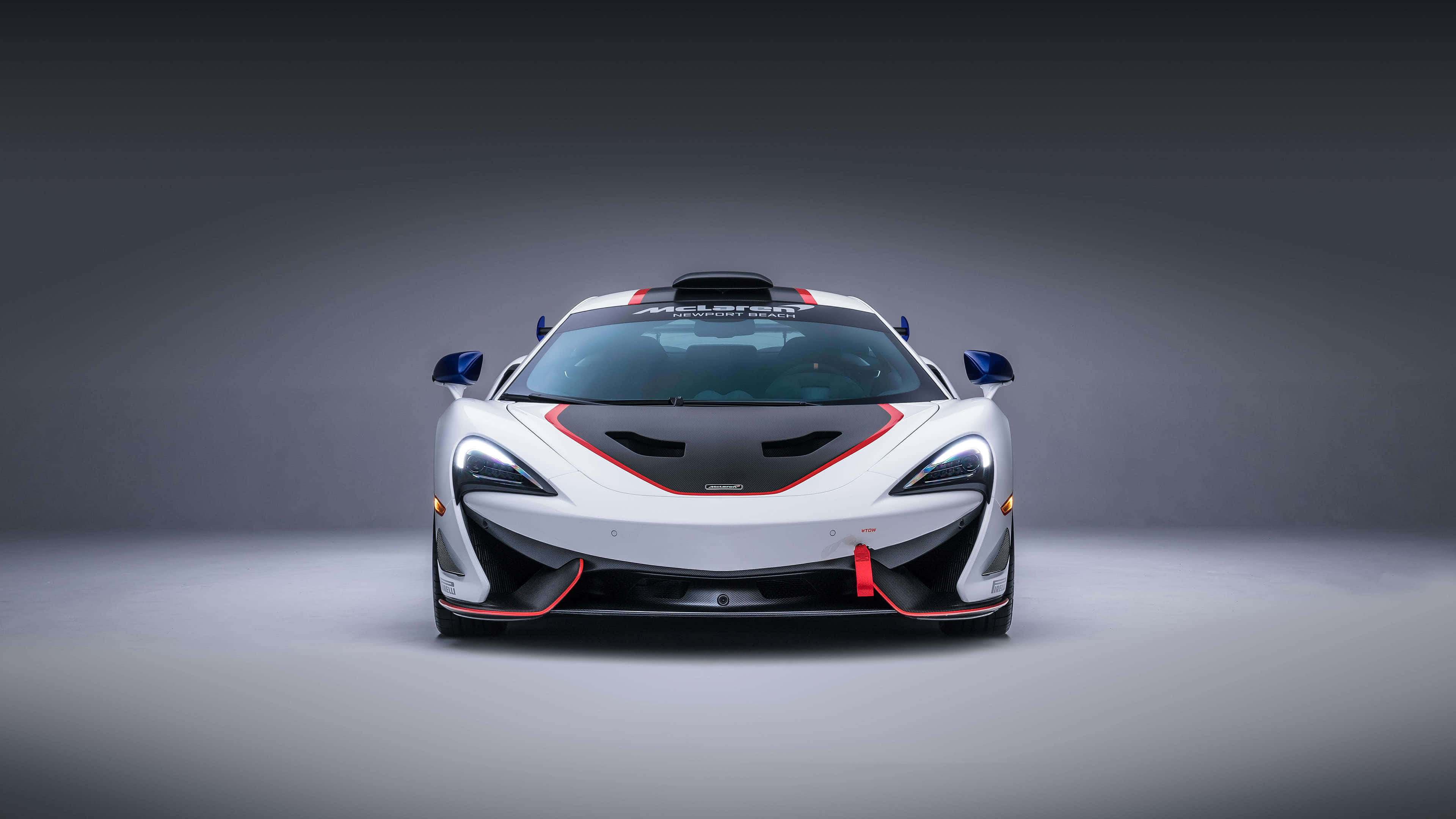 麥拉倫 桌布 壁紙 — 一輛白色McLaren賽車，帶有紅色和黑色點綴，在灰色背景下的工作室燈光下向前凝視。