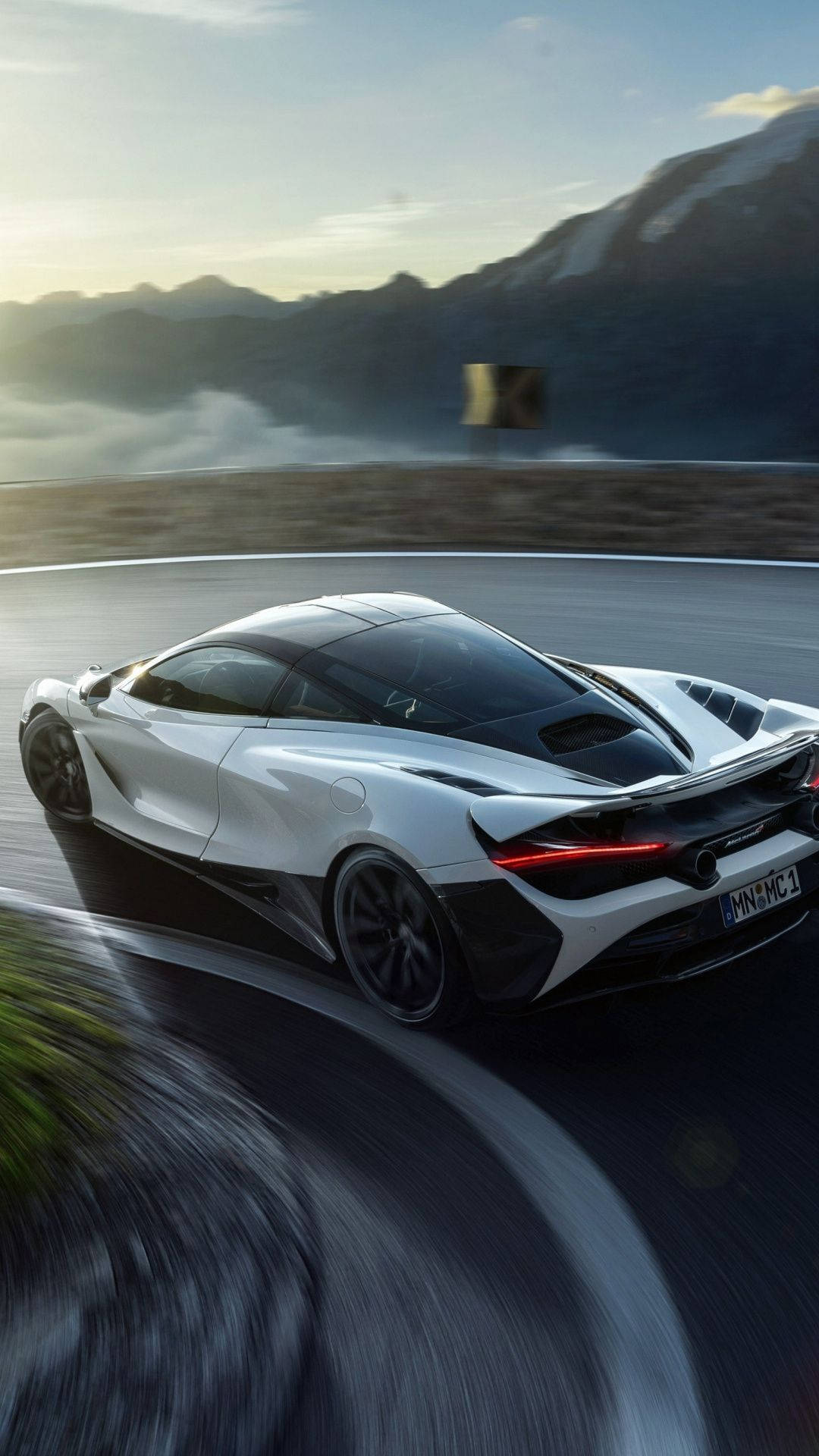跑車 桌布 壁紙 — 一輛白色McLaren跑車在日落時分沿著蜿蜒的山路奔馳，背景有動態模糊和霧氣繚繞的山峰。