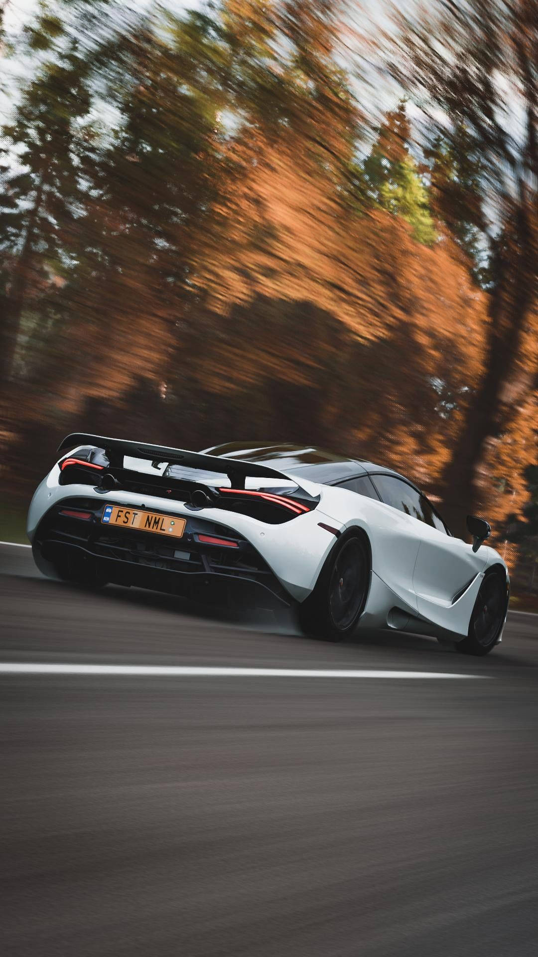 自然 桌布 壁紙 — 一輛白色McLaren跑車在秋樹於溫暖金色光線中模糊掠過的道路上疾馳。