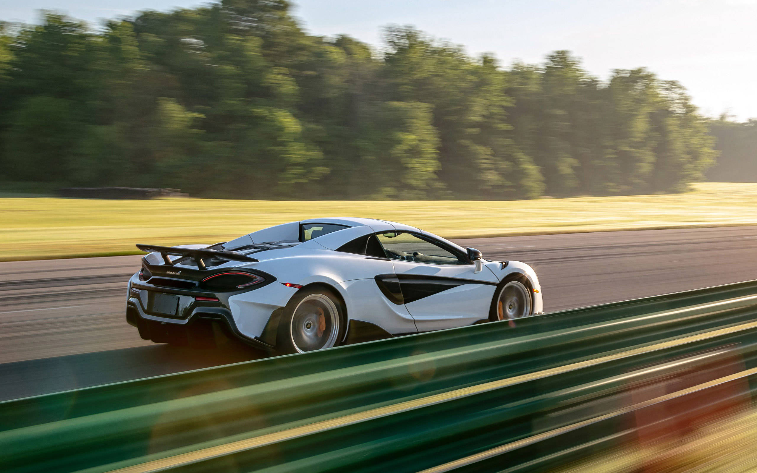 跑車 桌布 壁紙 — 一輛白色McLaren跑車在賽道上疾馳，背景有模糊的綠樹和護欄。