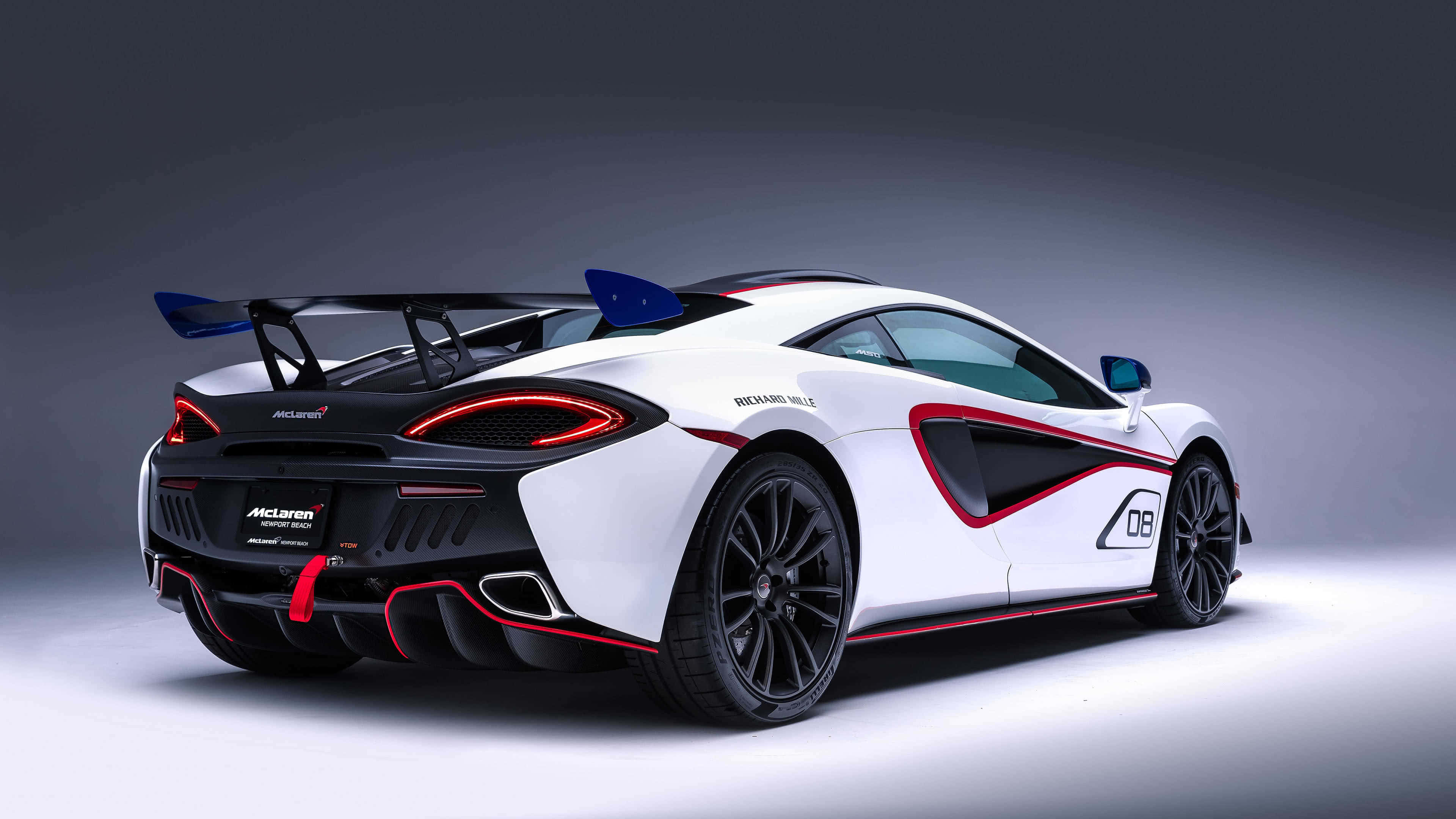 麥拉倫 桌布 壁紙 — 一輛白色McLaren跑車帶有紅色點綴和大型尾翼，從後方四分之三角度展示，背景為深灰色工作室背景。