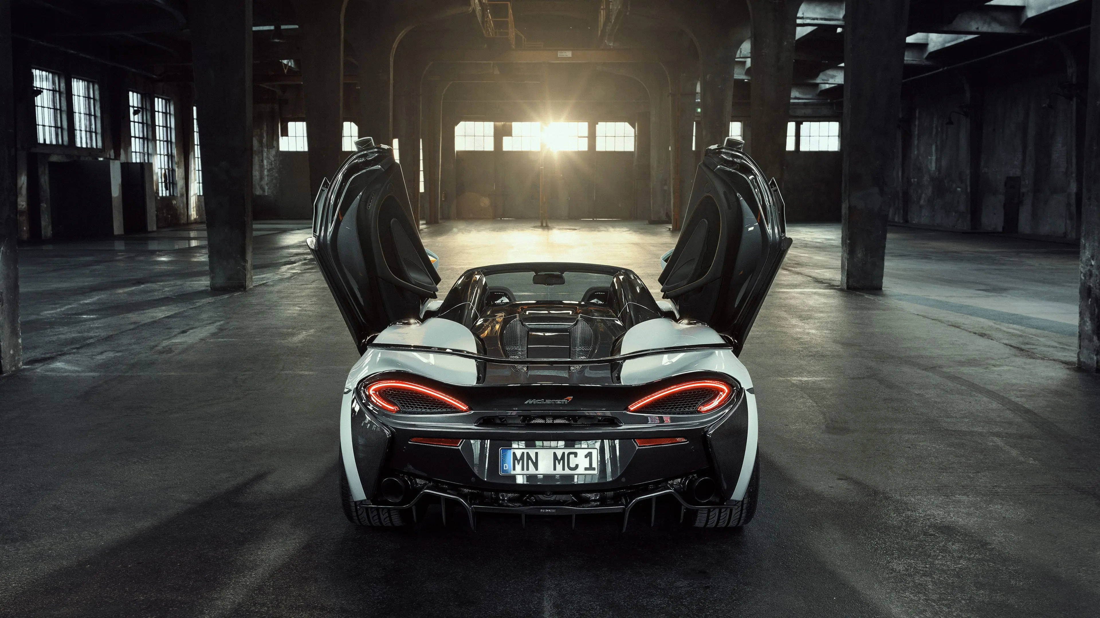 跑車 桌布 壁紙 — 一輛白色McLaren跑車打開蝴蝶門，停在陽光普照的廢棄倉庫中，紅色尾燈在粗糙的混凝土上發光。