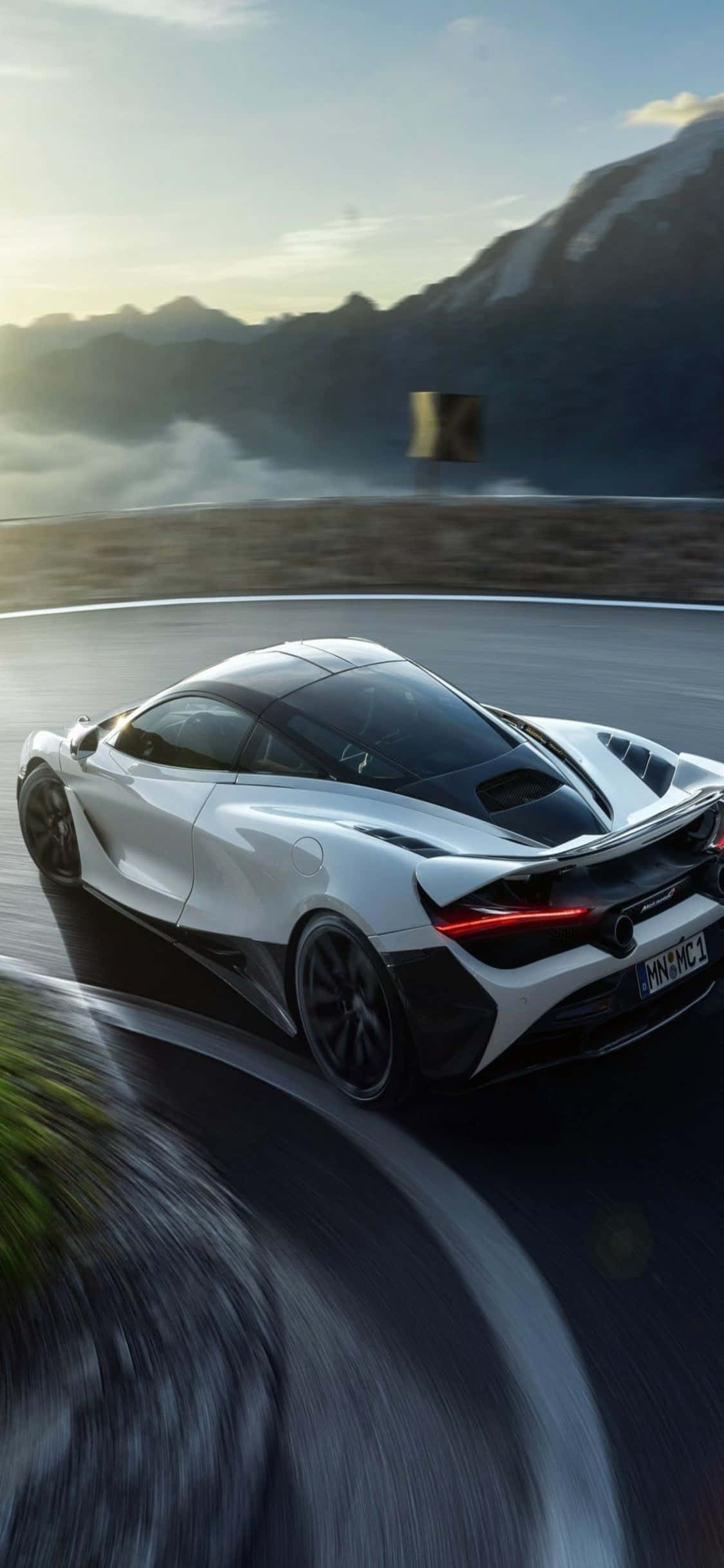 iPhone Xs Mclaren 720s 桌布 壁紙 — 一輛白色McLaren跑車沿著蜿蜒的山路疾馳，背景是模糊的動感和霧氣繚繞的山峰。