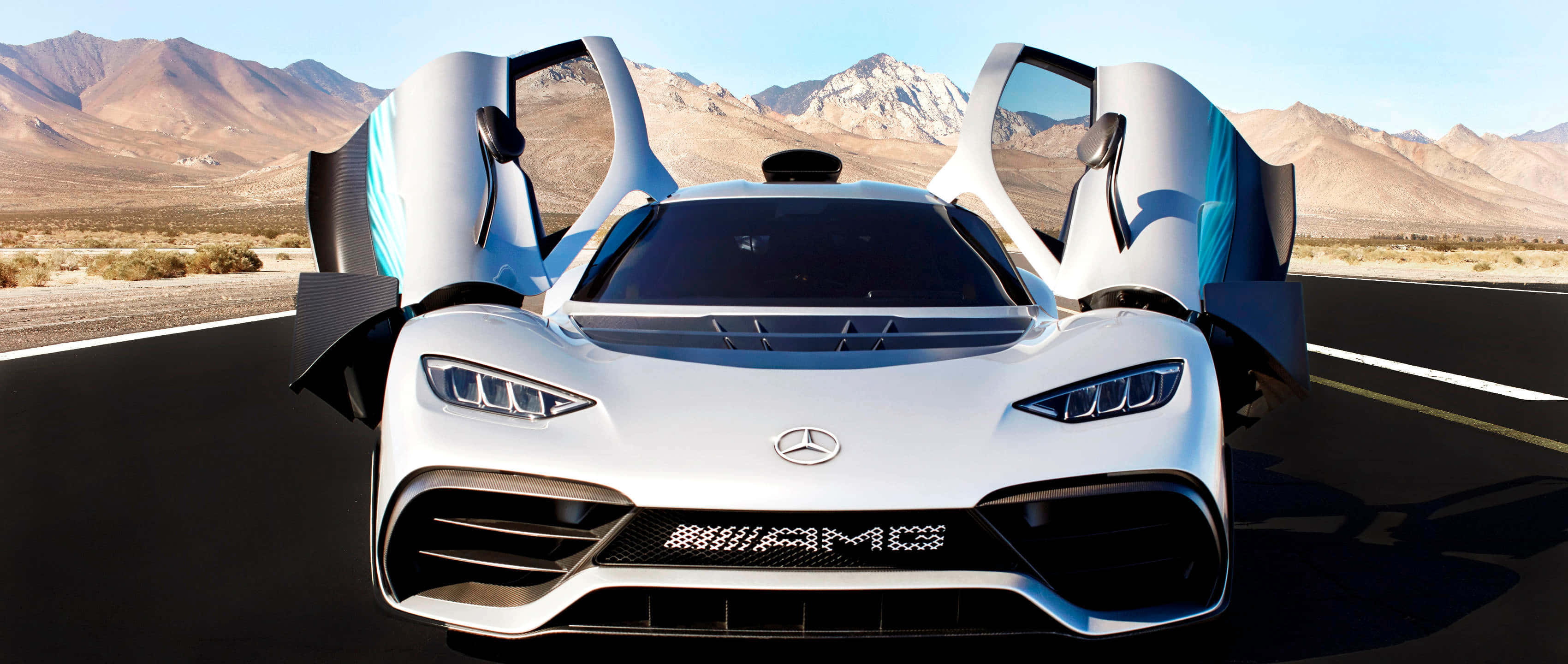 Mercedes 桌布 壁紙 — 一輛白色Mercedes-AMG One超級跑車，鷗翼車門打開，停在沙漠公路上，背景是崎嶇的山脈，天空清澈湛藍。
