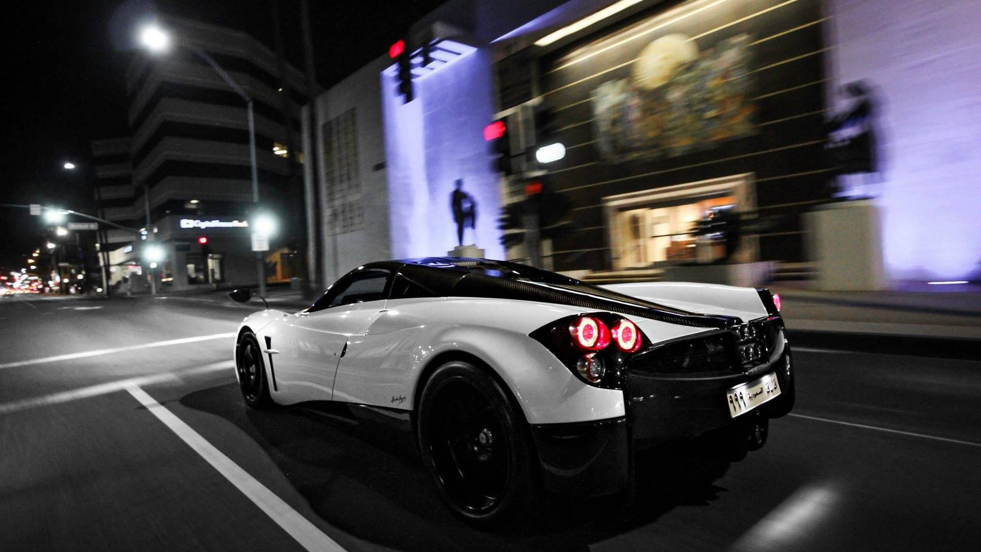 帕加尼 桌布 壁紙 — 一輛白色Pagani Huayra在夜晚霓虹燈閃爍的街道上飛馳，背景建築物呈現動態模糊效果。