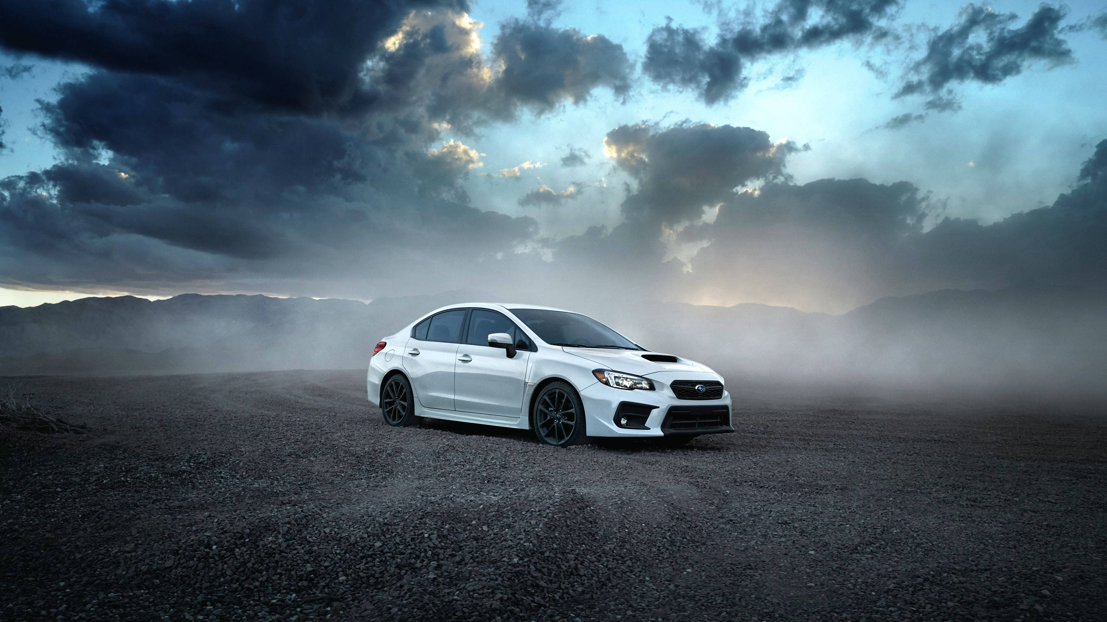 Subaru 桌布 壁紙 — 一輛白色Subaru WRX STI獨自佇立在碎石平原上，天空佈滿暴風雲和霧氣，呈現戲劇性的暮色。