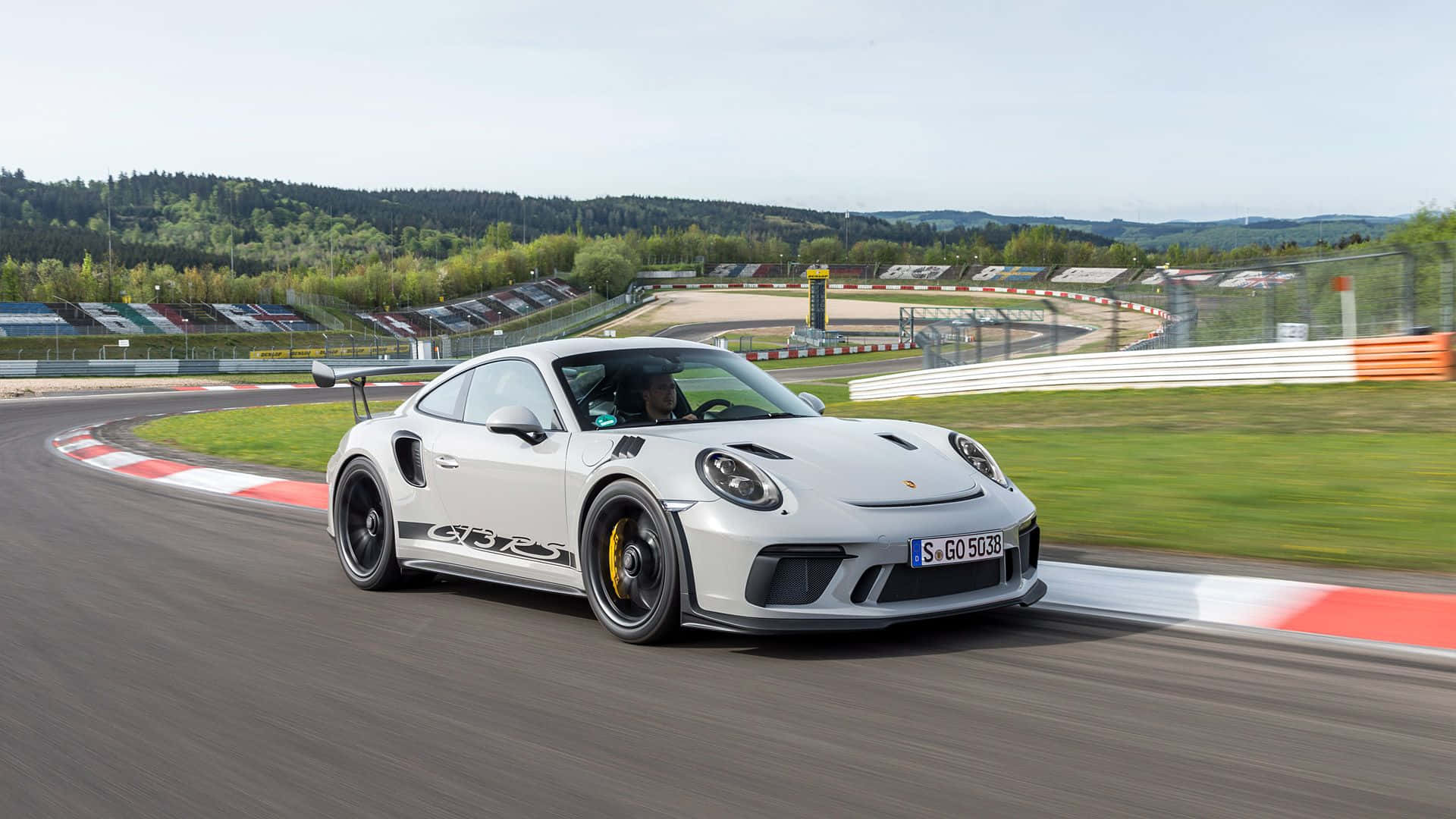保時捷 桌布 壁紙 — 一輛白色保時捷911 GT2 RS在賽道彎道高速行駛，背景是模糊的綠色山丘和看台。