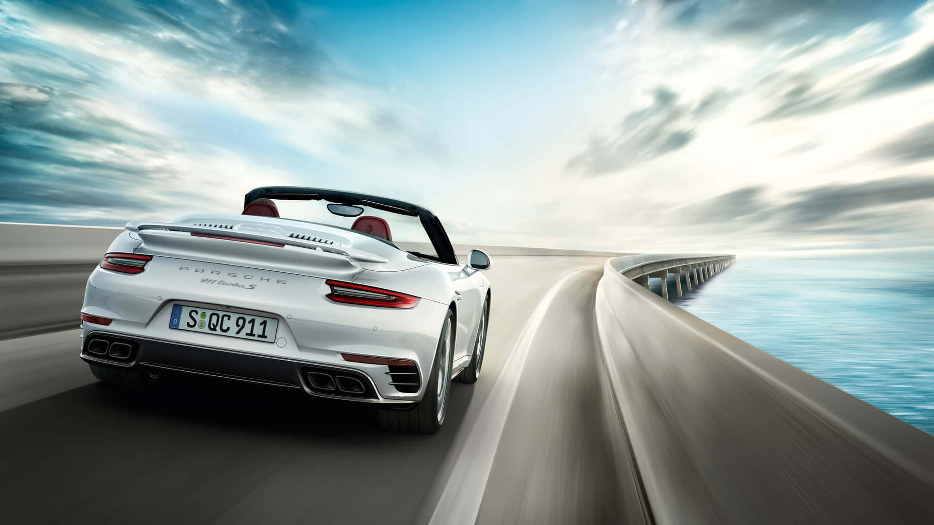 保時捷 桌布 壁紙 — 一輛白色保時捷911 Turbo S敞篷跑車在動態天空下沿著海岸高速公路奔馳，呈現模糊動態效果。